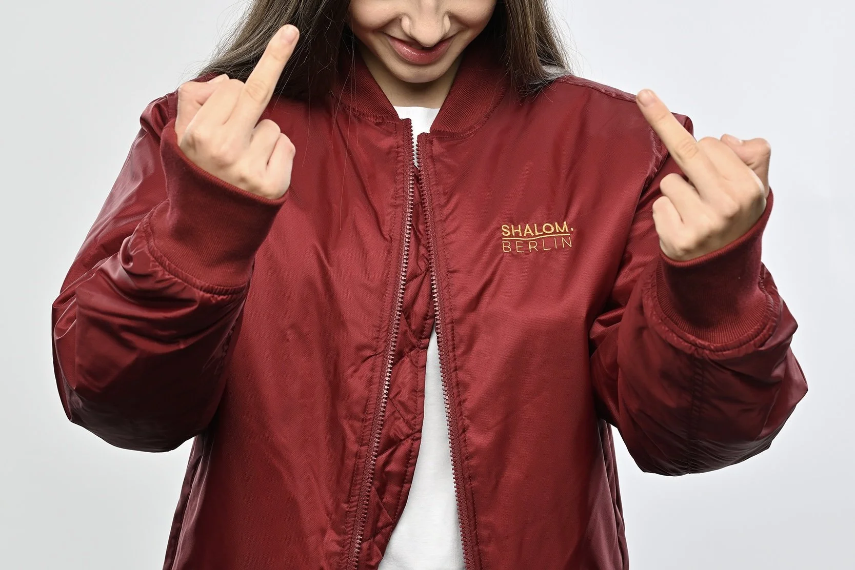 Girl wearing a bordeaux red bomber jacket with stitched golden logo "SHALOM.BERLIN"