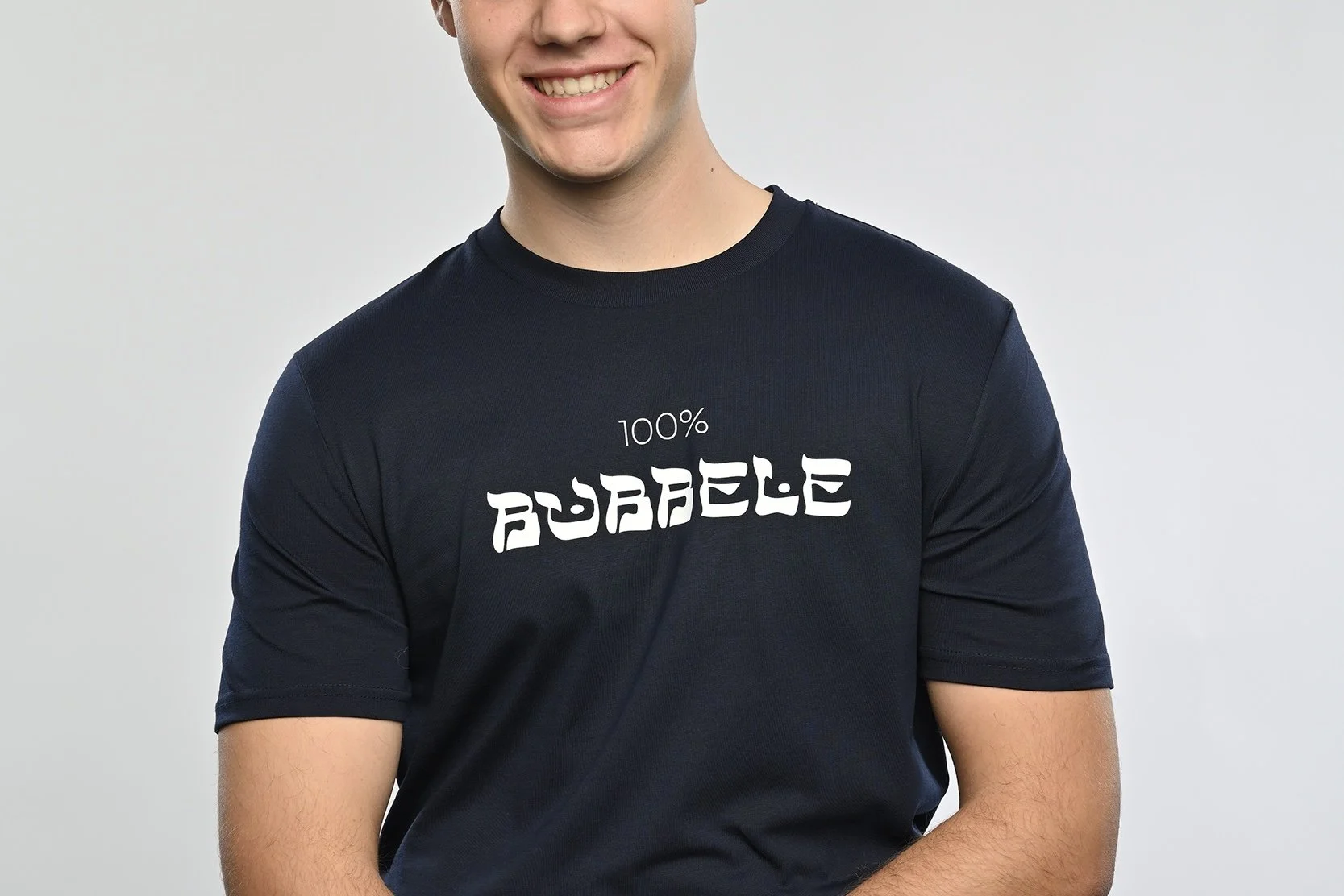Ein junger Mann trägt ein navy blaues T-Shirt der Marke SHALOM.BERLIN mit weissem Aufdruck "100% BUBBELE"