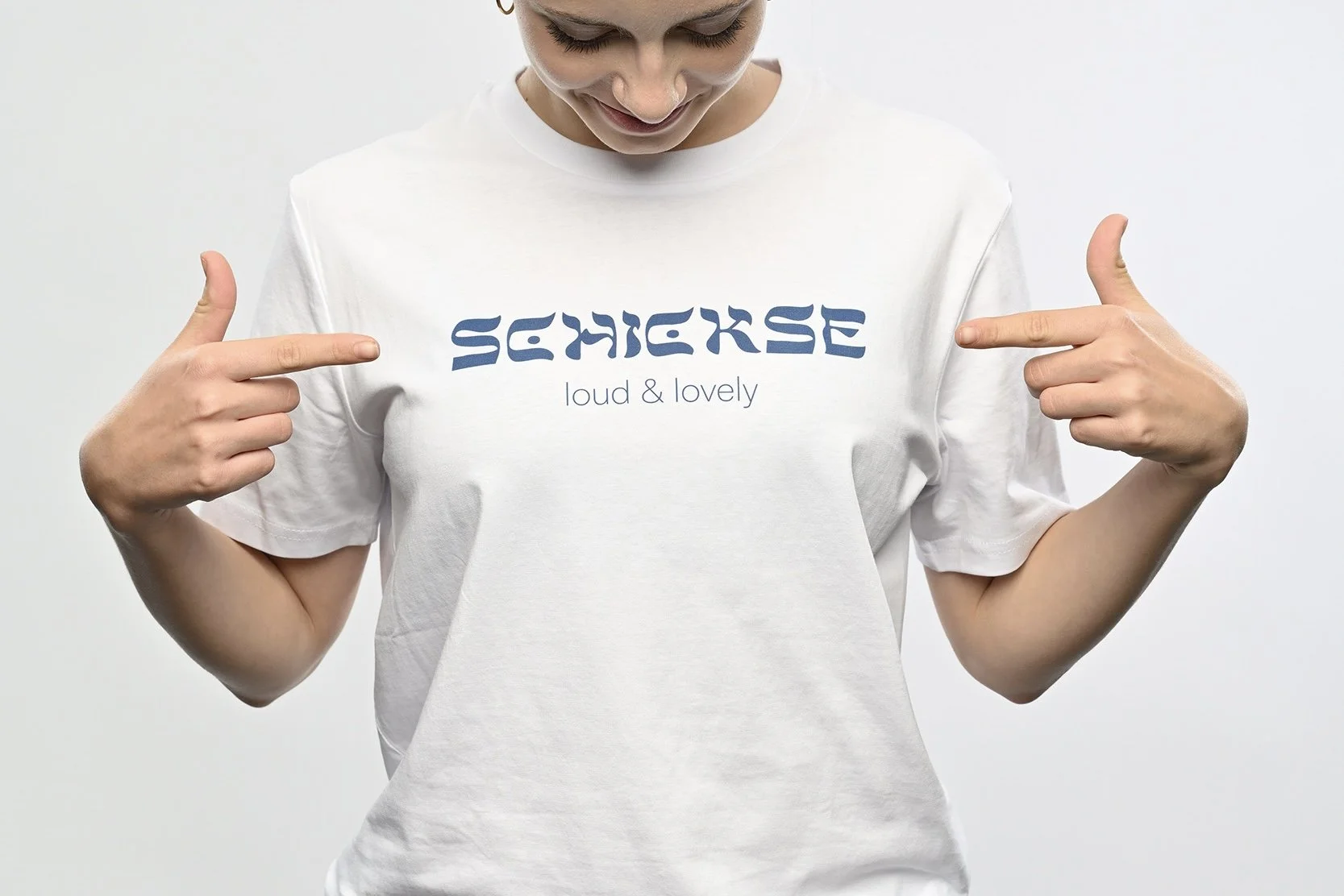Ein junger Mann trägt ein weisses T-Shirt der Marke SHALOM.BERLIN mit blauem Aufdruck "SCHICKSE loud and lovely"