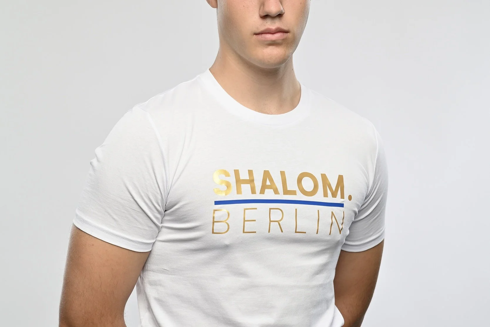 Ein junger Mann trägt ein weisses T-Shirt der Marke SHALOM.BERLIN mit blauem Aufdruck "SHALOM.BERLIN"