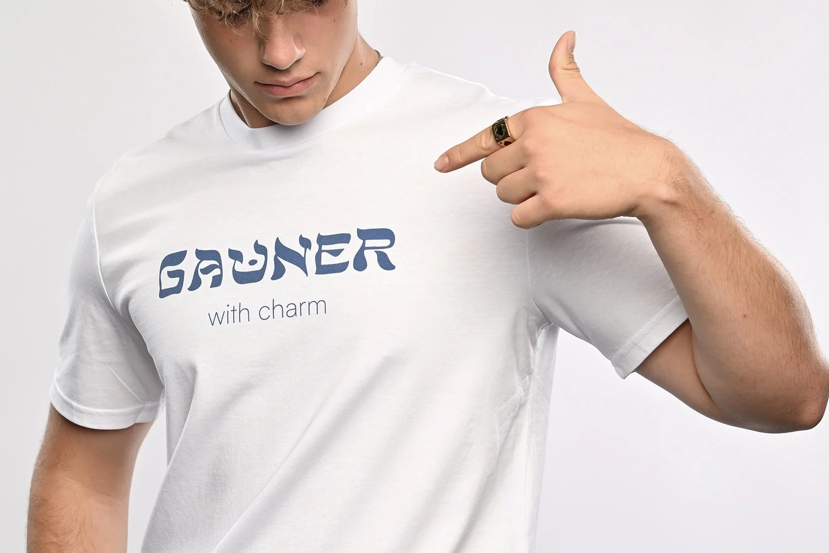 Ein junger Mann trägt ein weisses T-Shirt der Marke SHALOM.BERLIN mit blauem Aufdruck "GAUNER with charm"