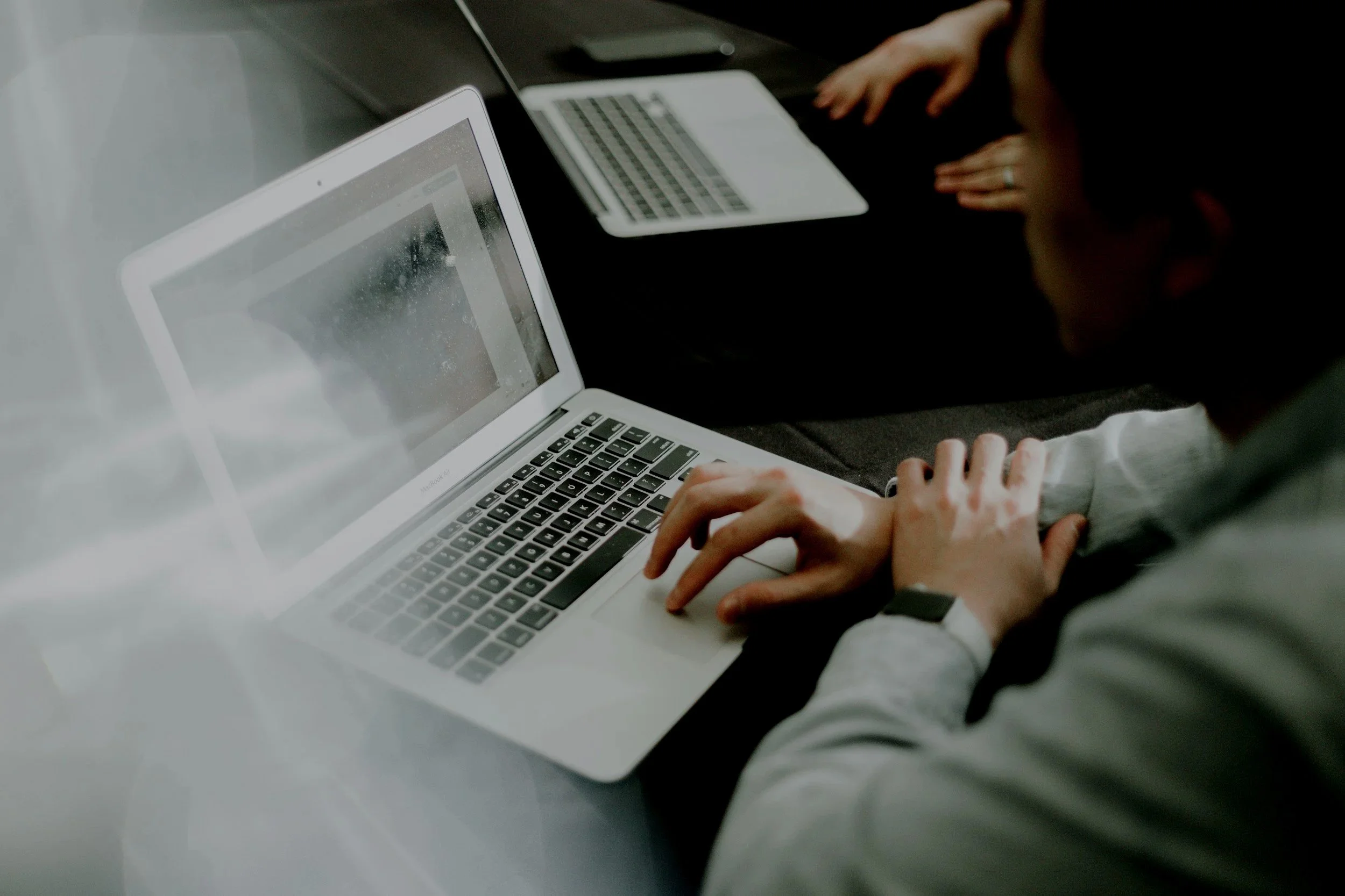 A person using a MacBook laptop at a meeting table with a second open laptop nearby.