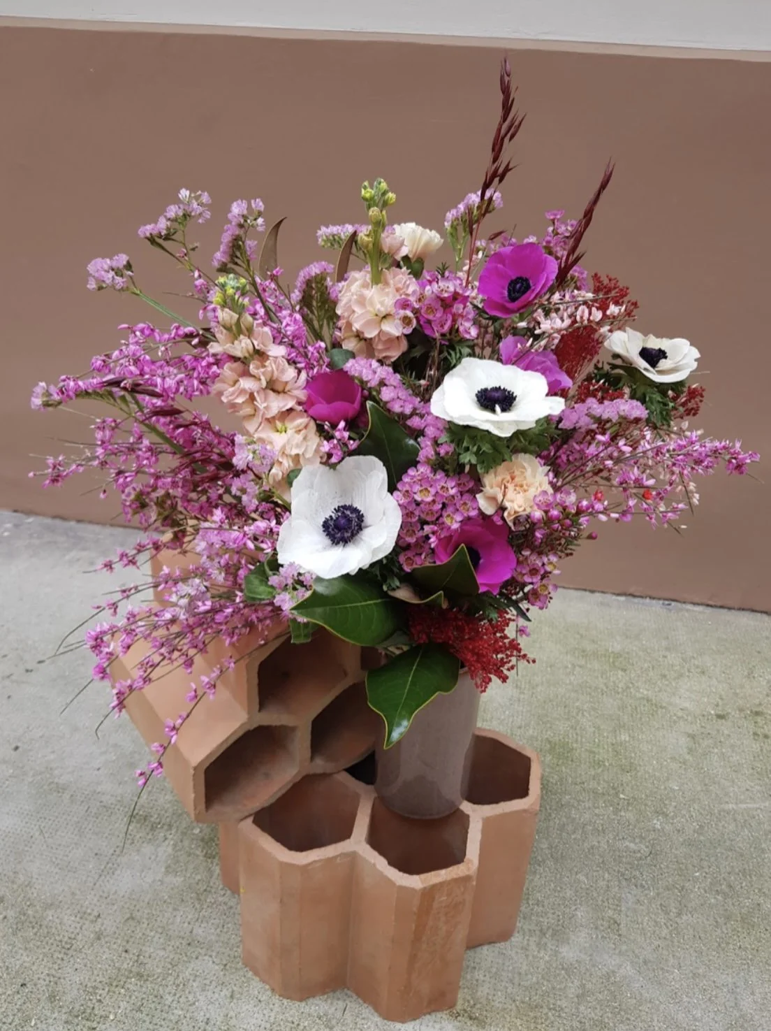 Un arrangement floral composé de fleurs roses, blanches et fucsias dans un vase placé sur une structure en briques en forme de tube à essai.