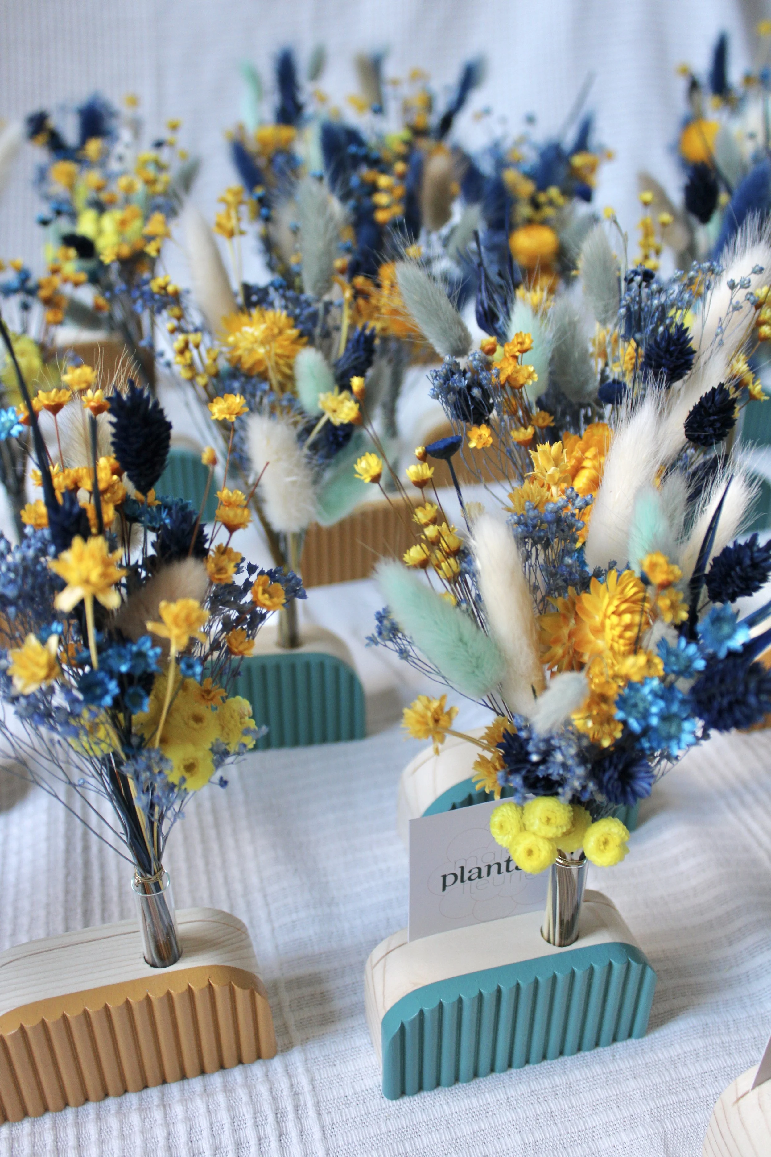 Bouquets de fleurs artificielles jaunes, bleues, vertes et blanches sur une table blanche.