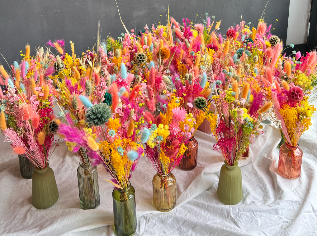 Bouquets de fleurs colorées dans différentes vases en verre sur une table drapée de tissu blanc