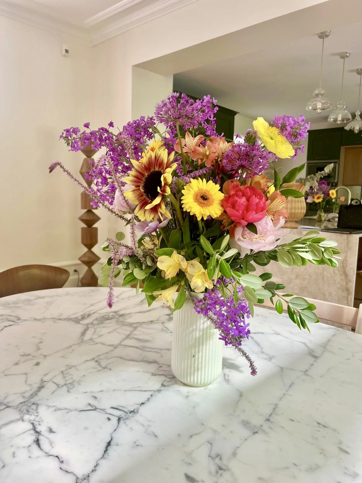 Un bouquet de fleurs colorées dans un vase blanc sur une table en marbre.