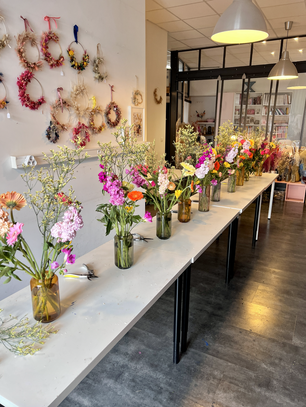 Table avec plusieurs vases remplis de fleurs colorées, mur décoré de couronnes de fleurs