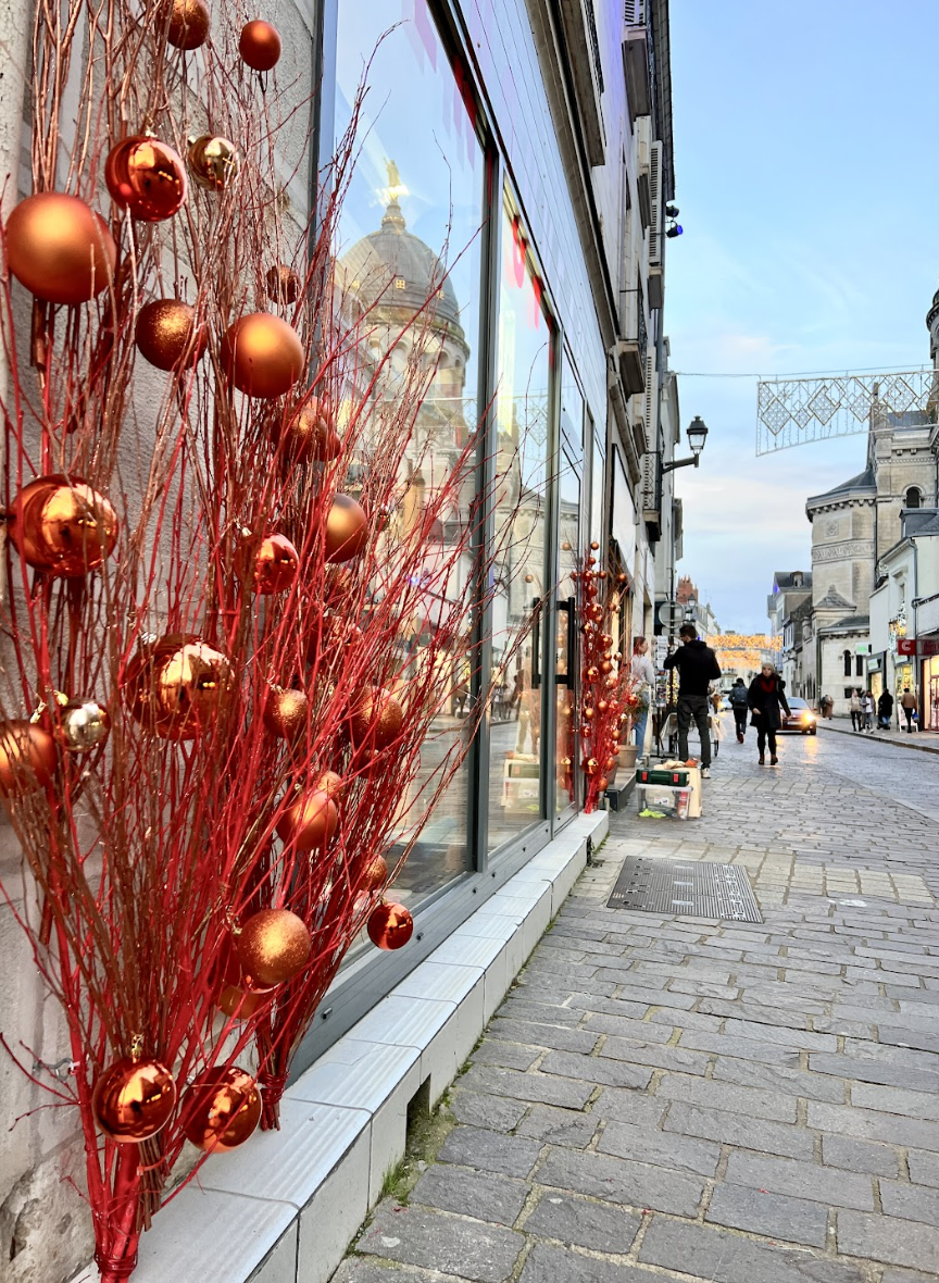 Décoration de Noël avec des branches rouges et des boules de Noël en or et rouge devant une vitrine d'un magasin sur une rue pavée