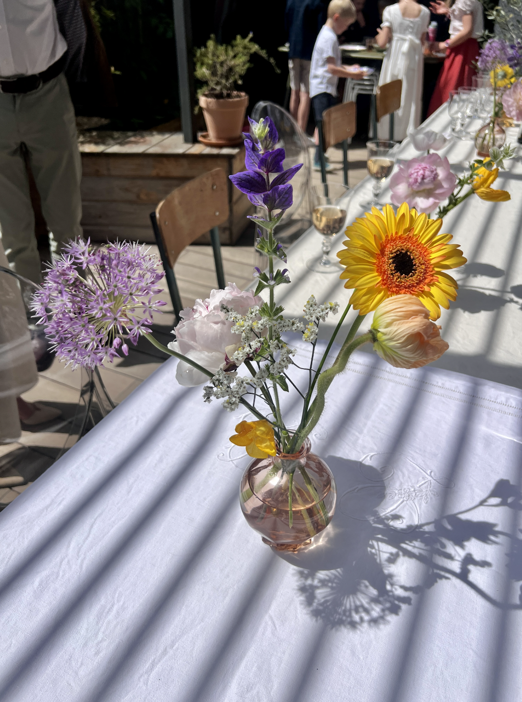 Un vase avec un bouquet de fleurs colorées sur une table blanche lors d'un événement en plein air.