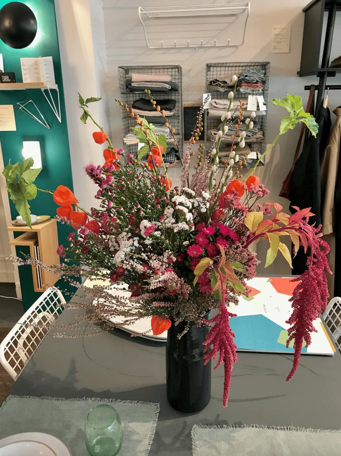 Un grand bouquet de fleurs colorées dans un vase noir sur une table, avec une salle de séjour en arrière-plan.