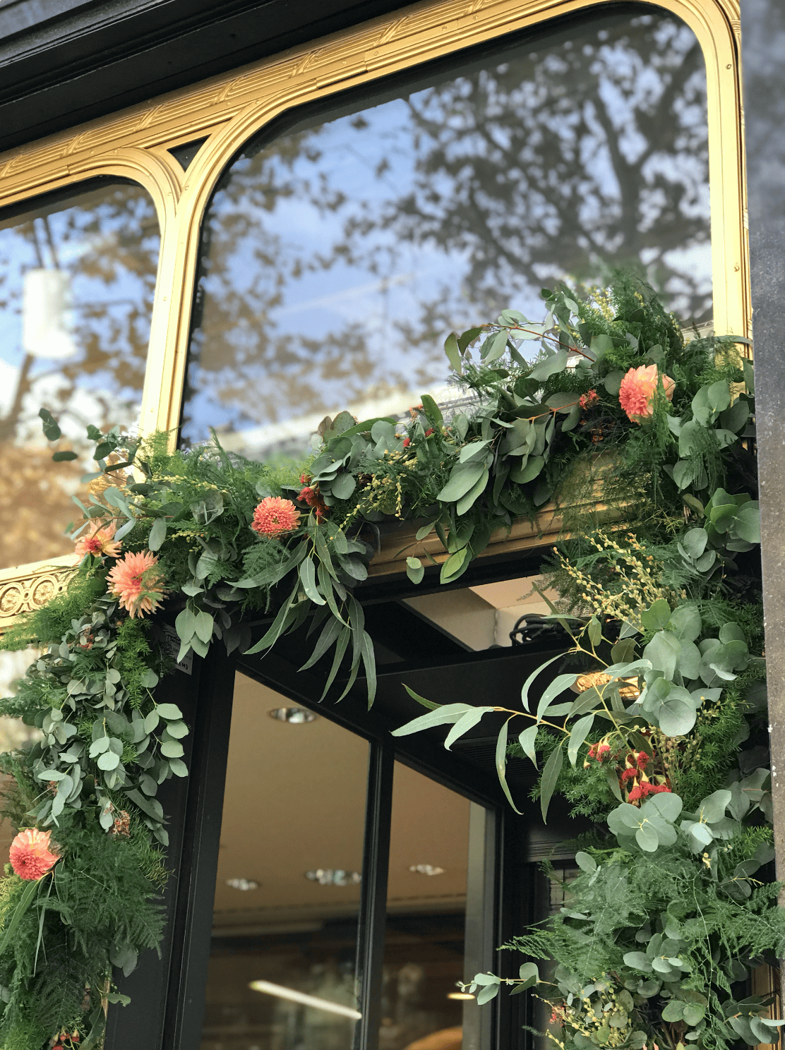 Décoration florale composée de feuillages verts et de fleurs roses, ornant une grande fenêtre en verre avec cadre doré.