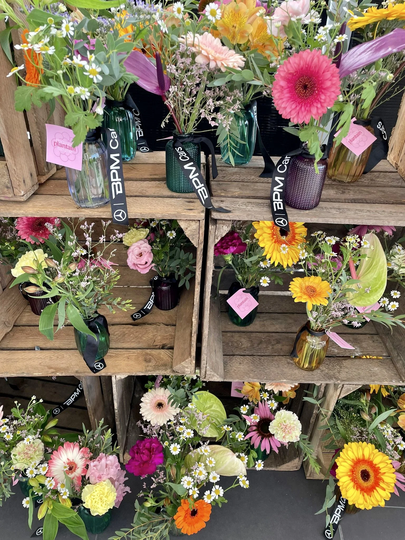 Mélange de bouquets de fleurs colorées dans des vases en verre sur des étagères en bois.