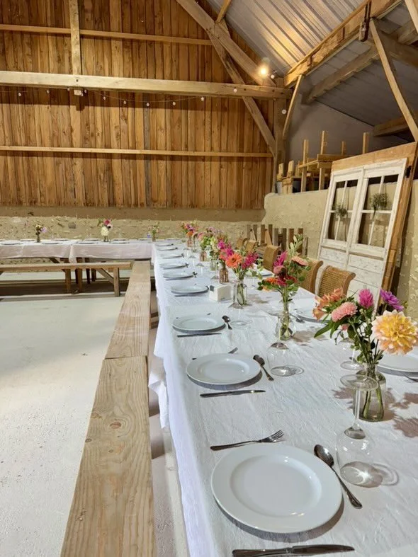 Table dressée avec des assiettes, des couverts et des vases avec des fleurs dans un ambiance de ferme ou de grange en bois.