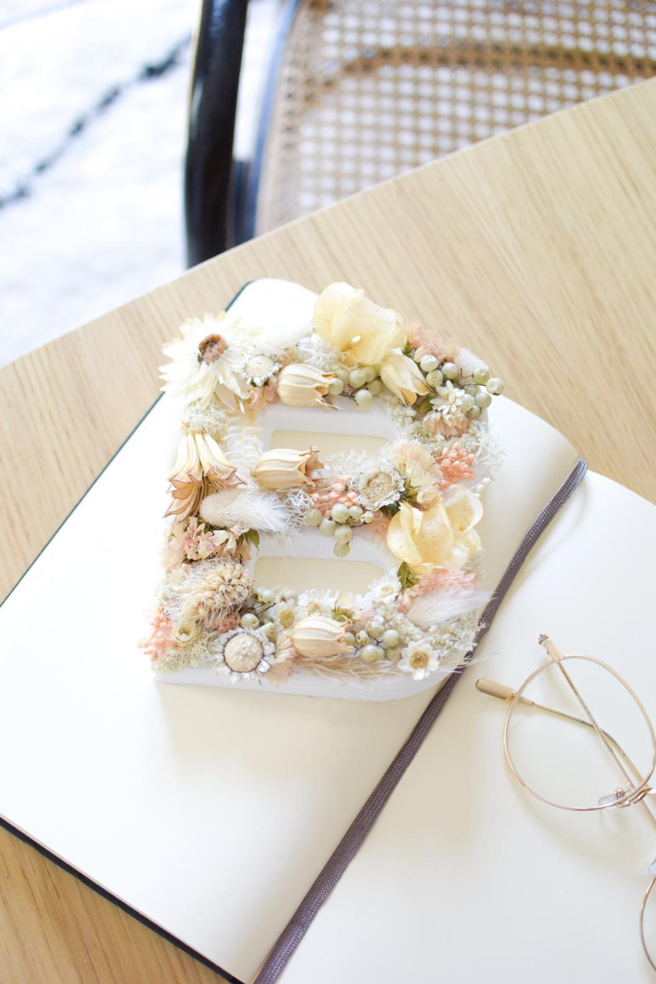 Gâteau en forme de numéro 8 décoré de fleurs pastel, placé sur un livre ouvert, avec des lunettes rondes à côté.