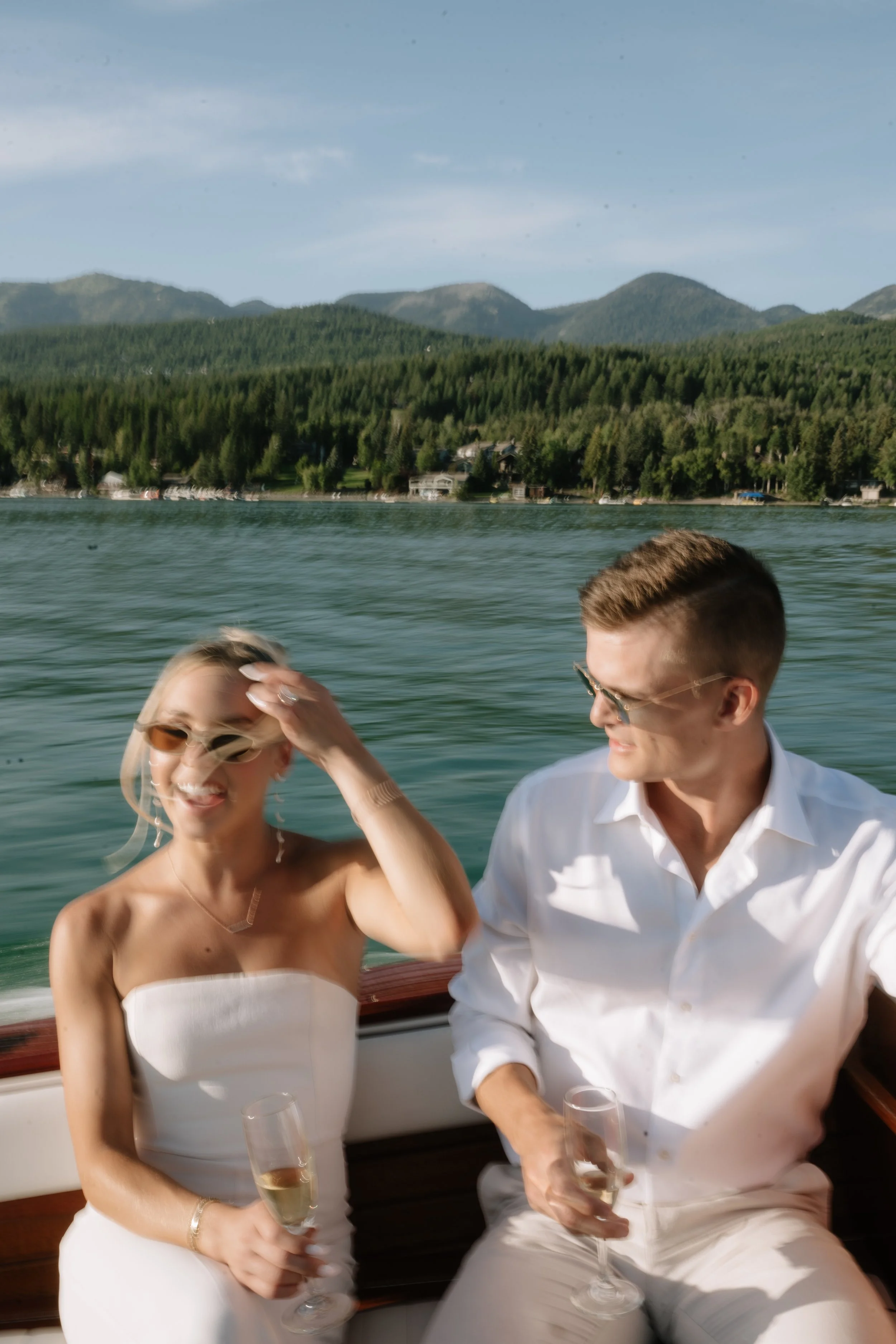 Couple enjoying a romantic wooden boat ride on Whitefish Lake at Whitefish Lake Lodge, Montana, toasting with champagne, with Whitefish Mountain in the background.
