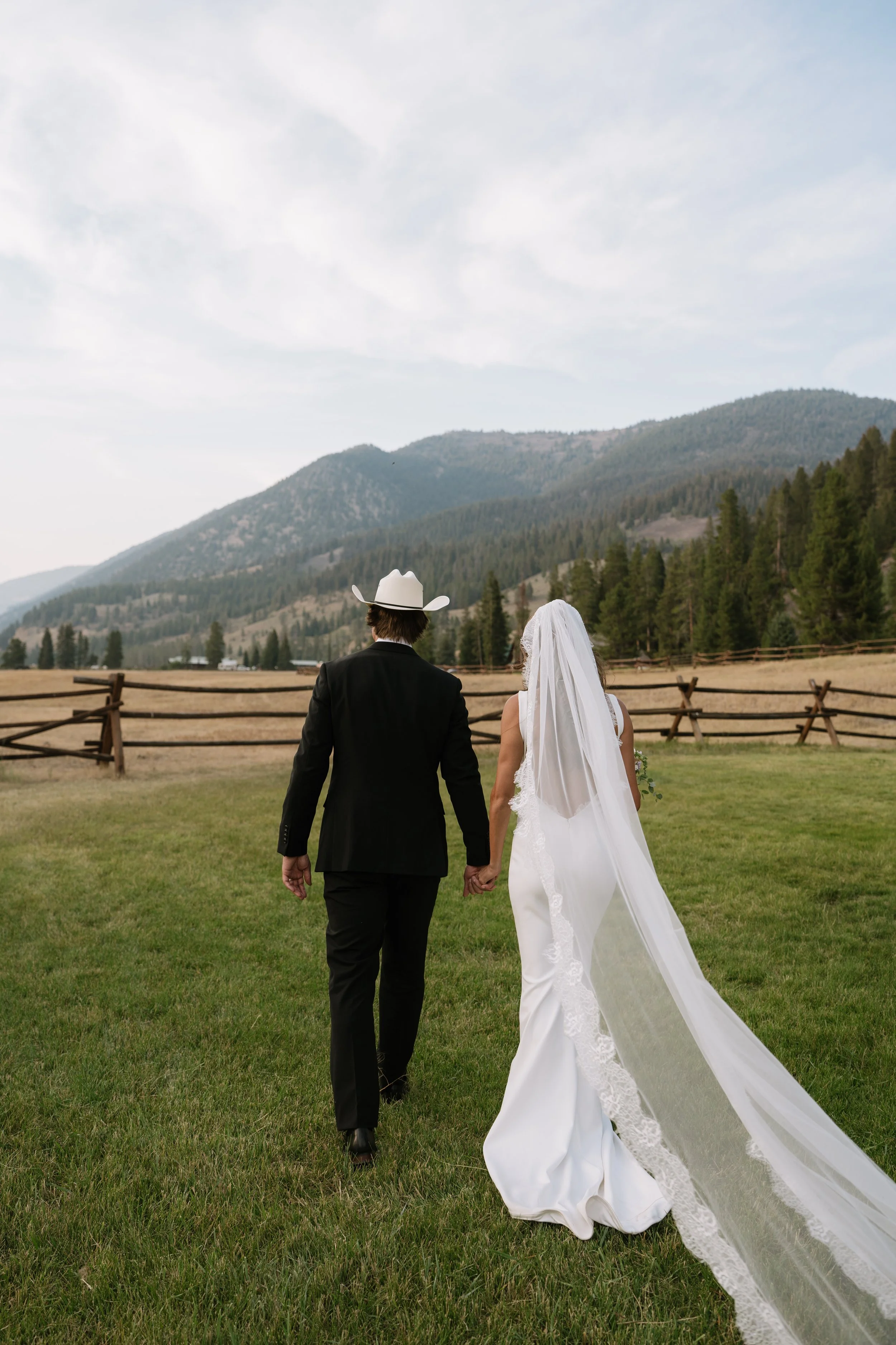 Bride and groom holding hands and walking through a grassy field during a Montana wedding at 320 Guest Ranch