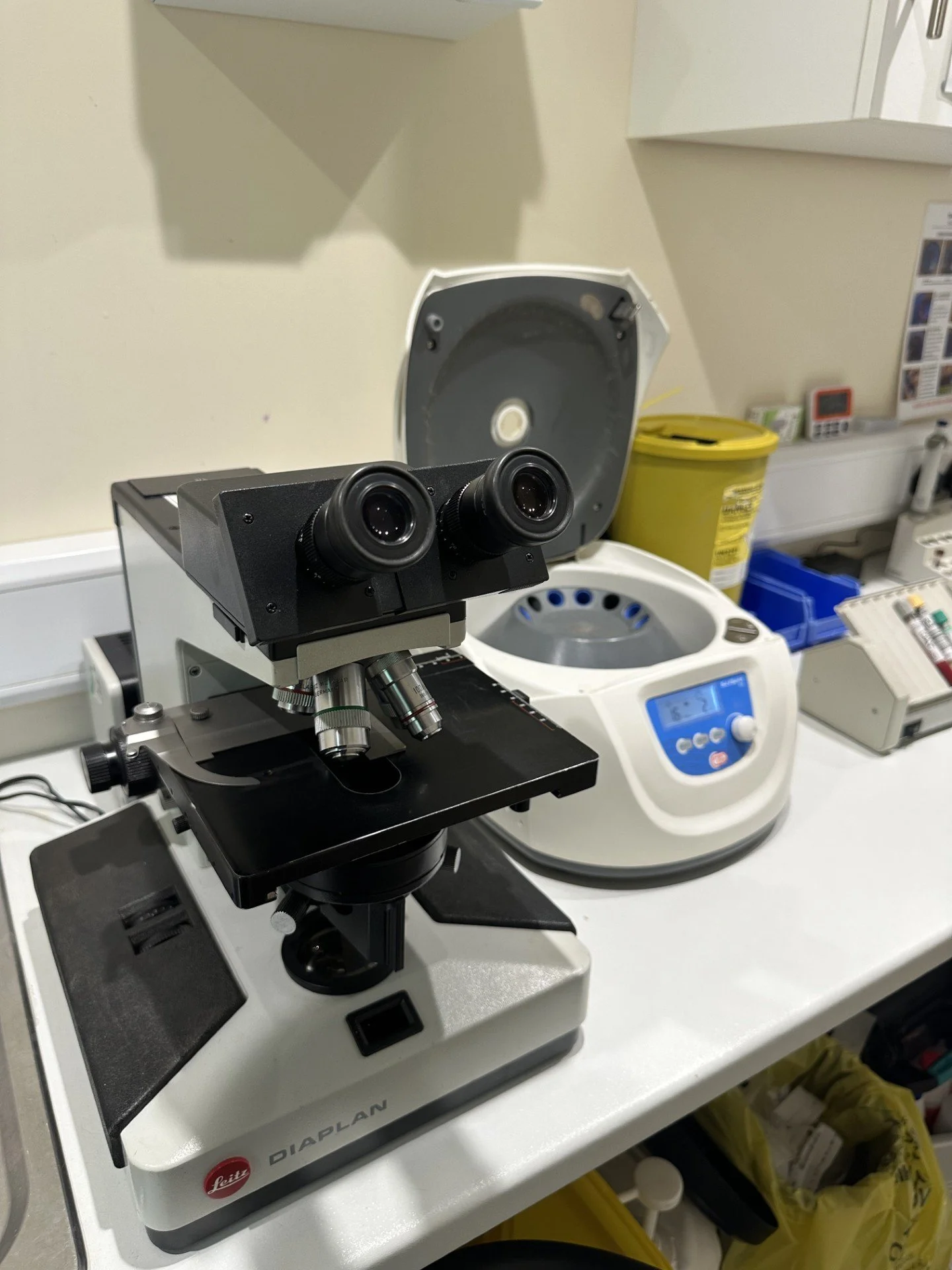 Microscope on a lab bench in a laboratory with a centrifuge and other lab equipment.