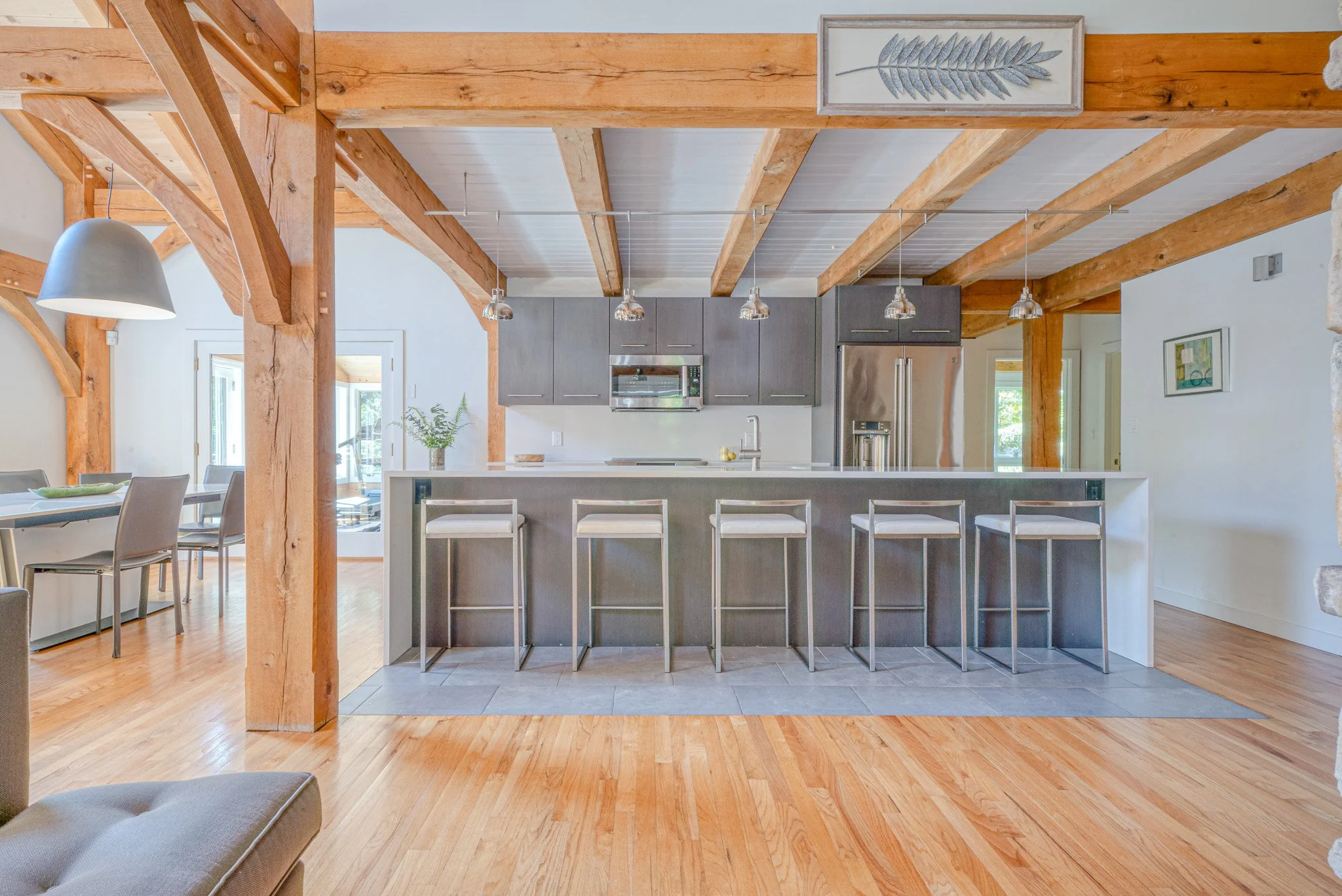 Modern kitchen with wooden beams, gray cabinets, stainless steel appliances, and a long kitchen island with five high chairs.