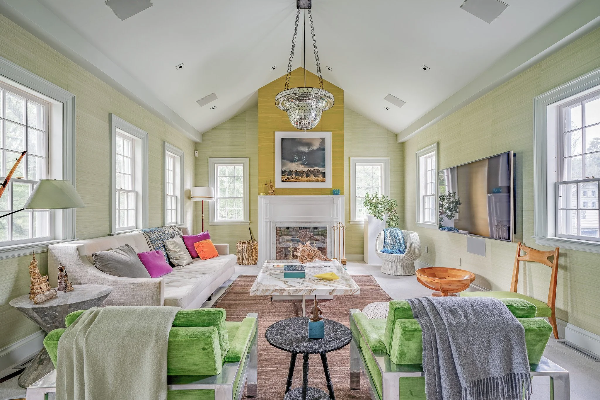 Bright living room with green walls, white ceiling, large windows, and modern furniture, including a white sofa, two green armchairs, a marble coffee table, and a flat-screen TV.