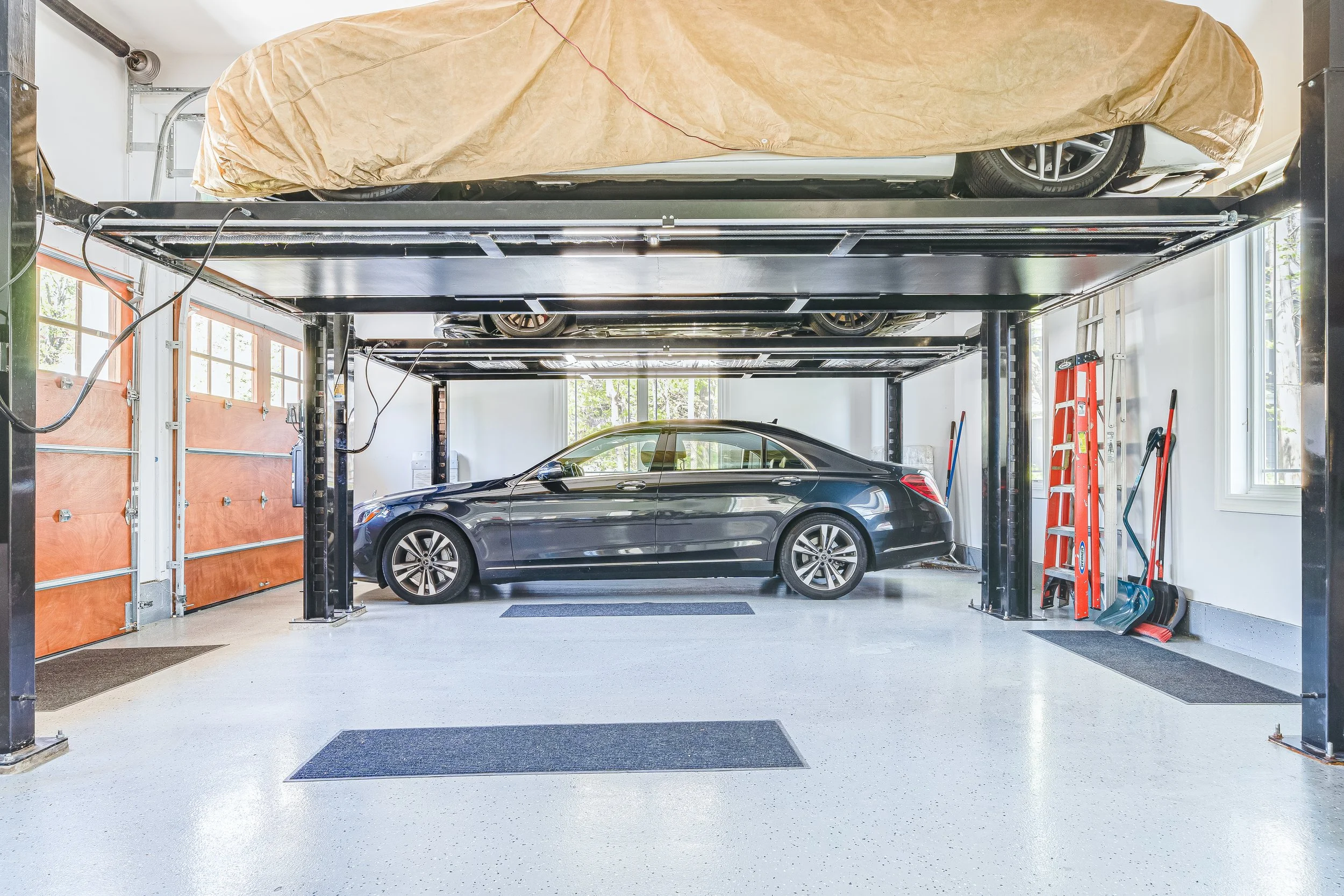 A black luxury car parked inside a clean, organized garage with two levels for vehicle storage.
