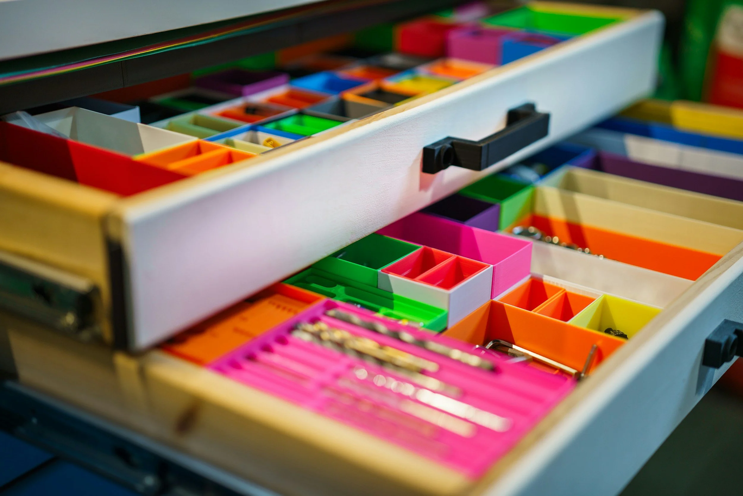Open drawers with colorful custom bins to maximize available storage space for office supplies such as paper clips, push pins, and sticky notes.
