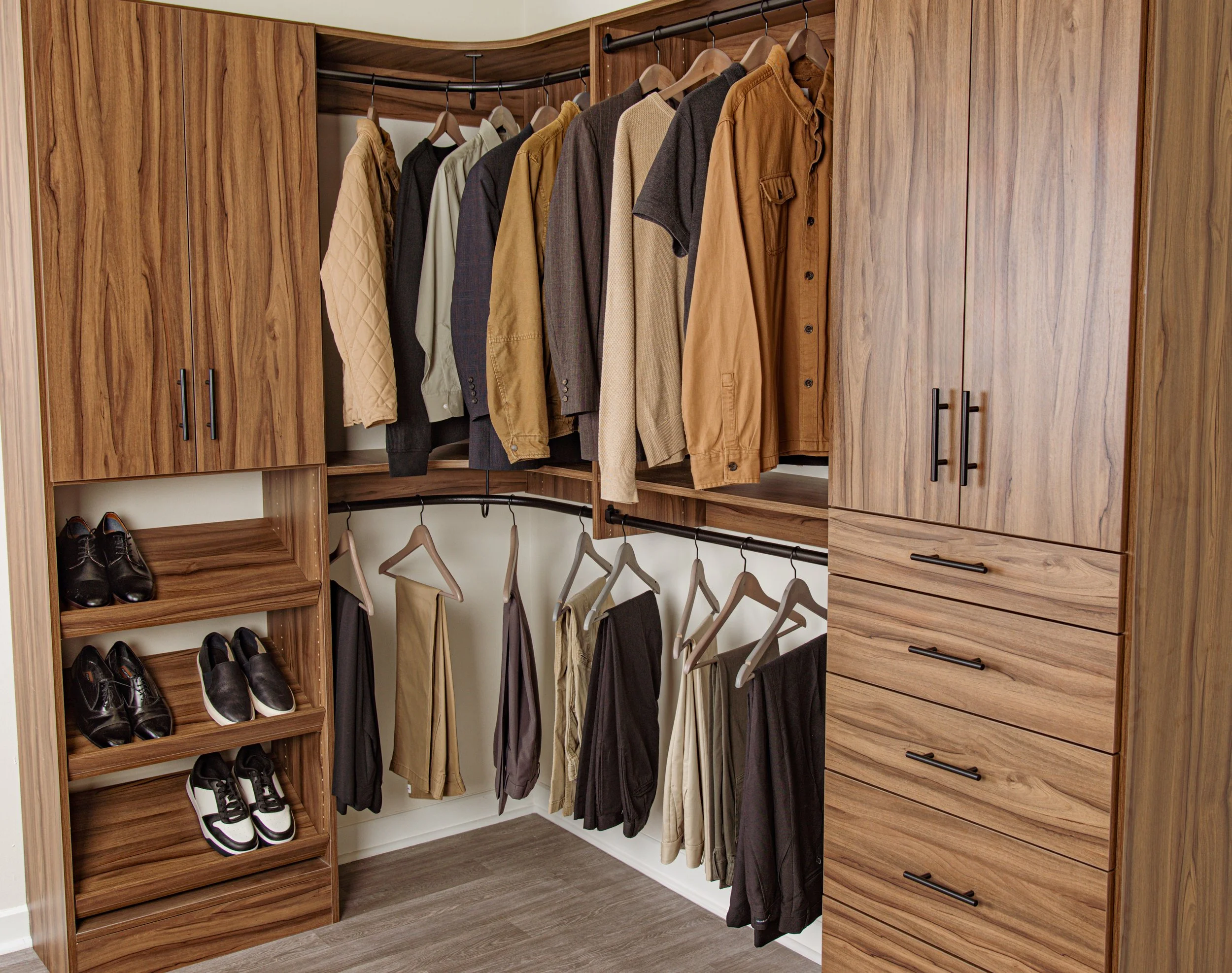 Walk-in custom closet with shelves, hanging rods, cabinets and drawers, shown in walnut with black hardware