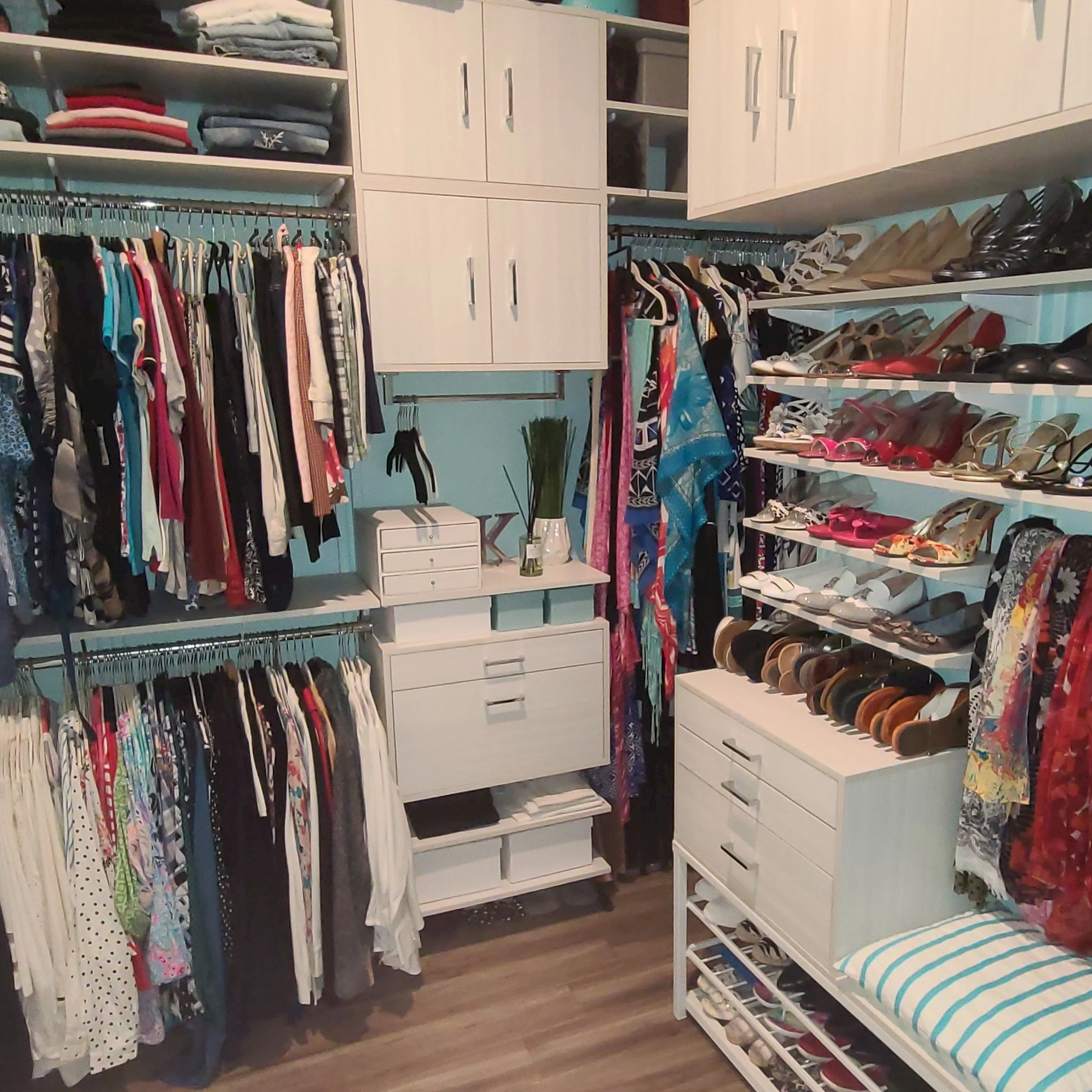 Photo of the first custom closet designed and installed by the Sprinklize president -h walk-in closet with organized clothing, shoes, and accessories. Clothes are hanging on racks, shoes are on shelves, and there are drawers and cabinets for storage.