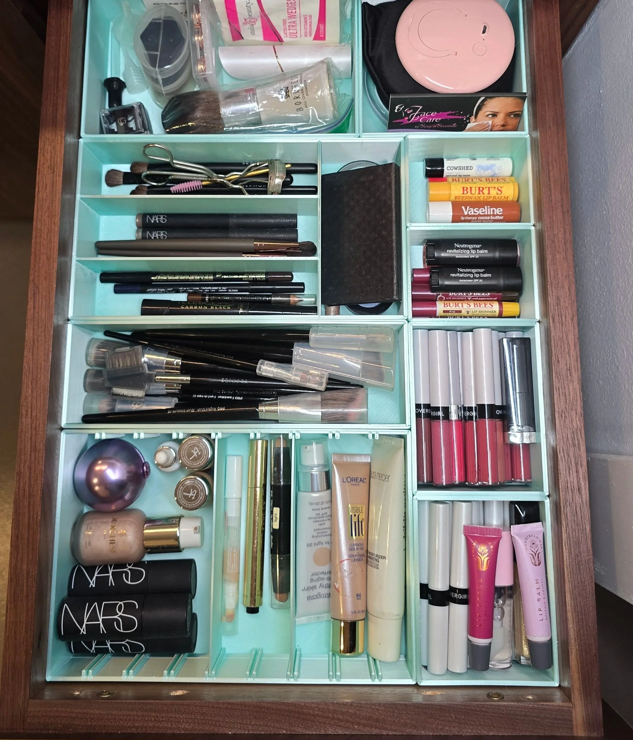 Organized makeup and skincare drawer with light blue custom bins to maximize storage space for brushes, lip balms, lipsticks, and other skincare products