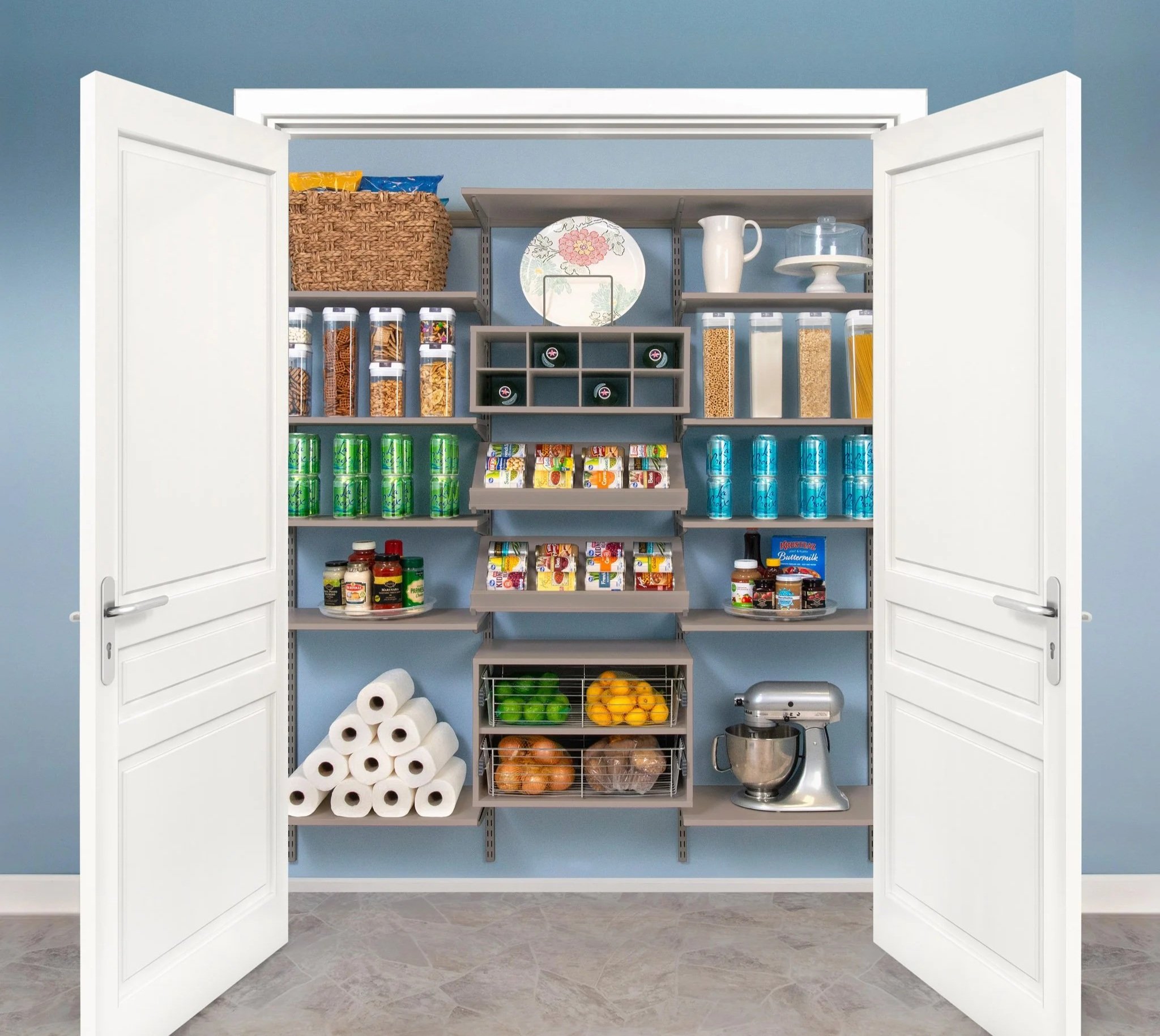 Organized reach-in pantry with adjustable shelves and cubbies filled with canned and jarred food, boxes, canisters, a fruit basket, paper towels, and a stand mixer, all behind open white double doors