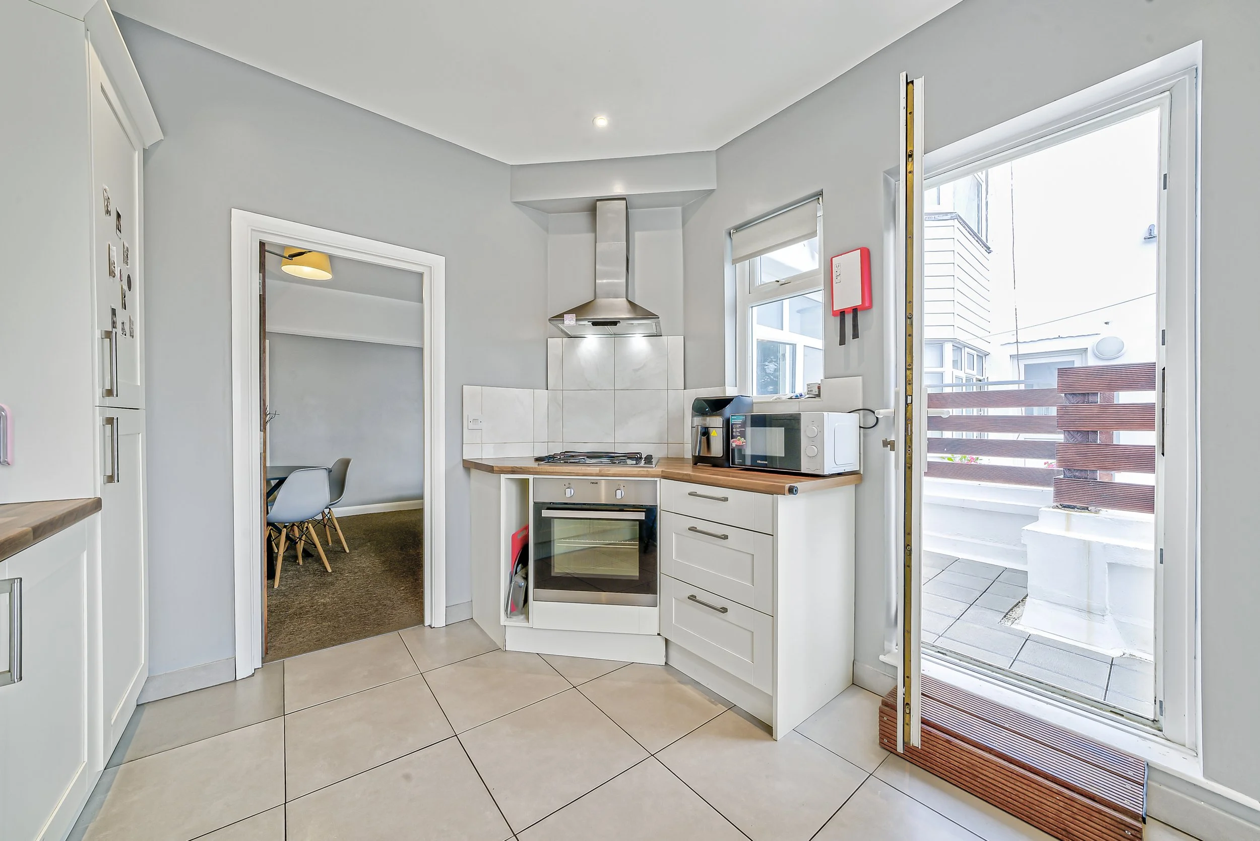 Modern kitchen with white cabinets, wooden countertops, stainless steel stove, oven, microwave, and coffee maker. There is a door leading outside to a small balcony or patio area.