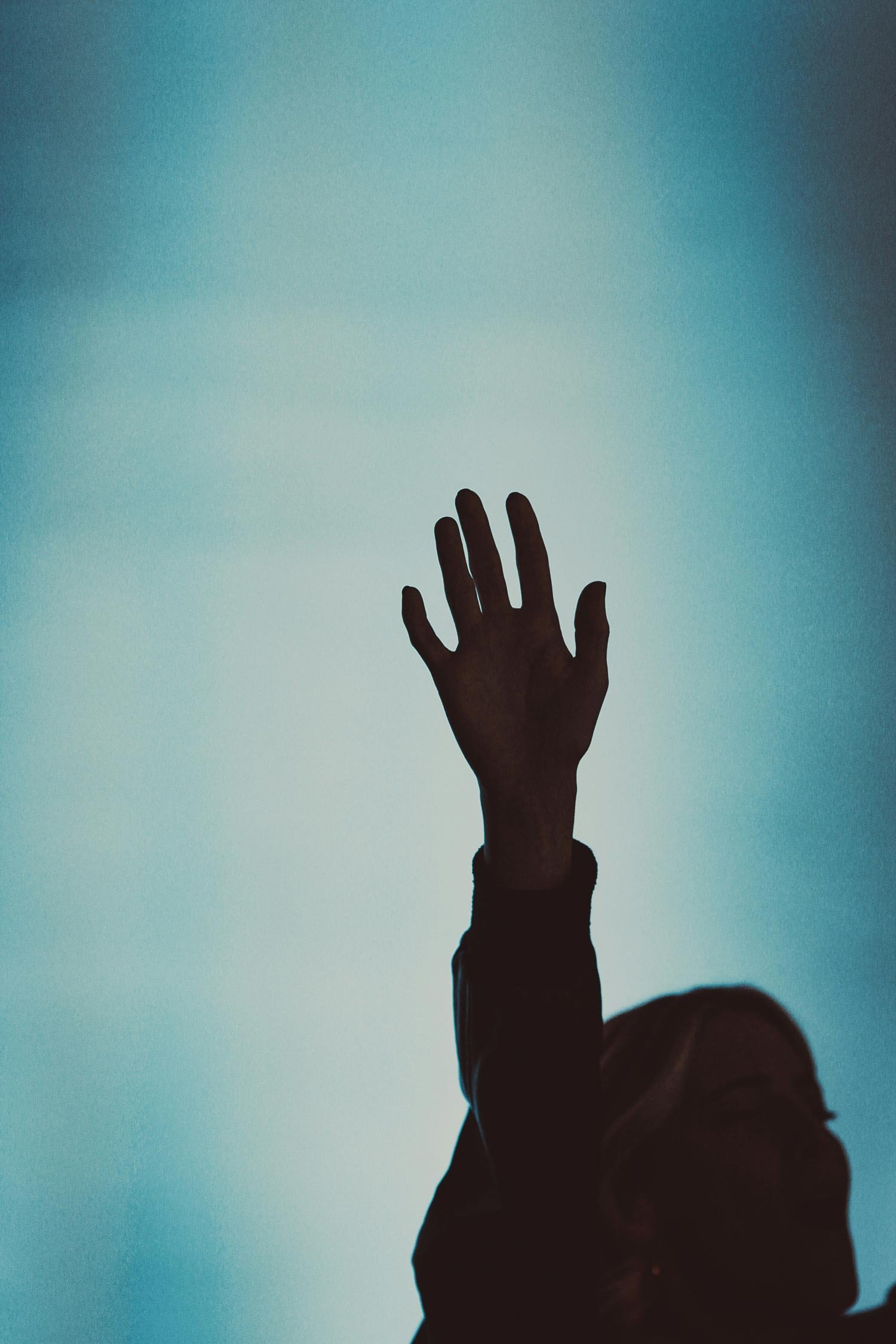 A person's silhouette with an arm raised, palm facing outward, against a gradient blue background.
