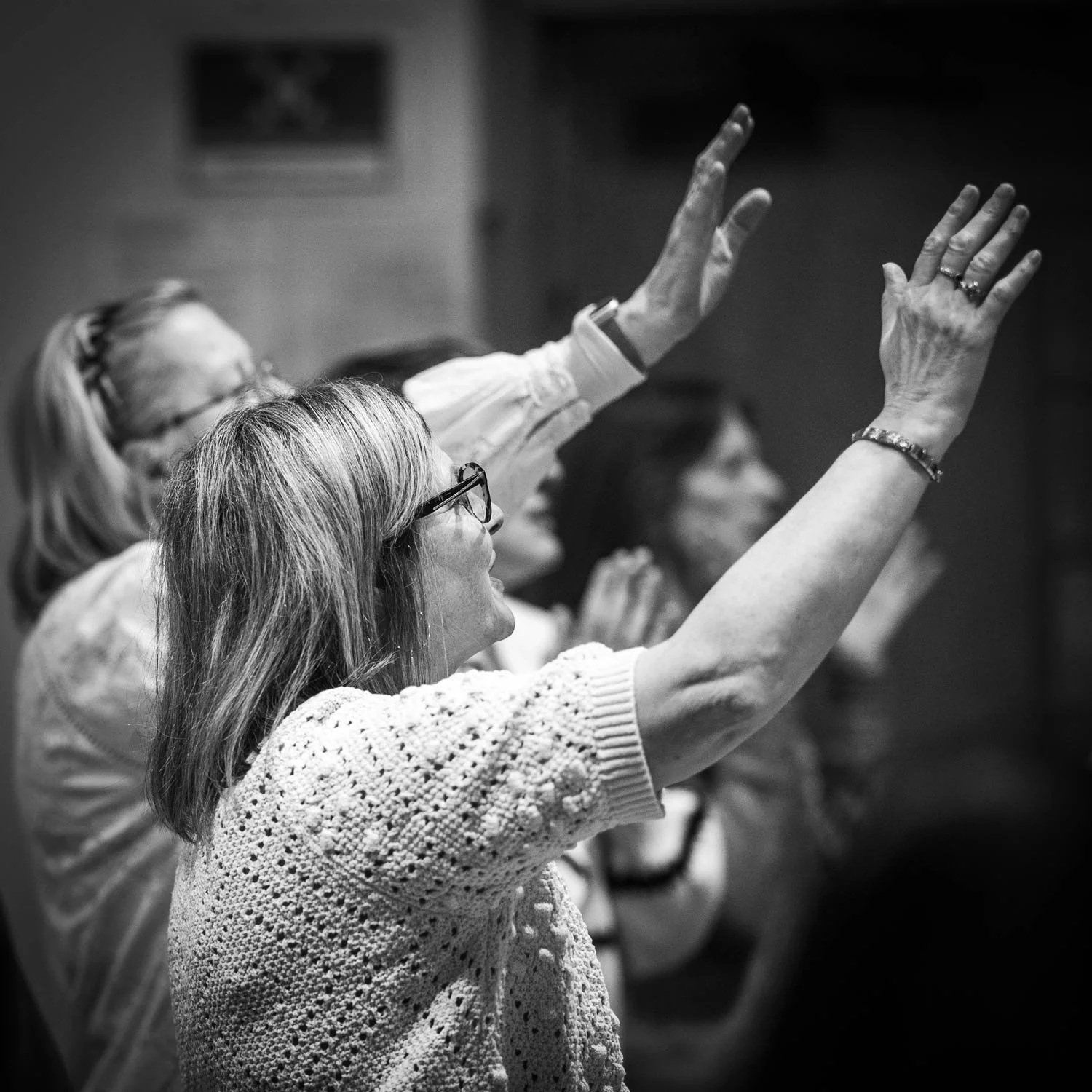 Group of women raising their hands during a meeting or religious service, black and white photo.