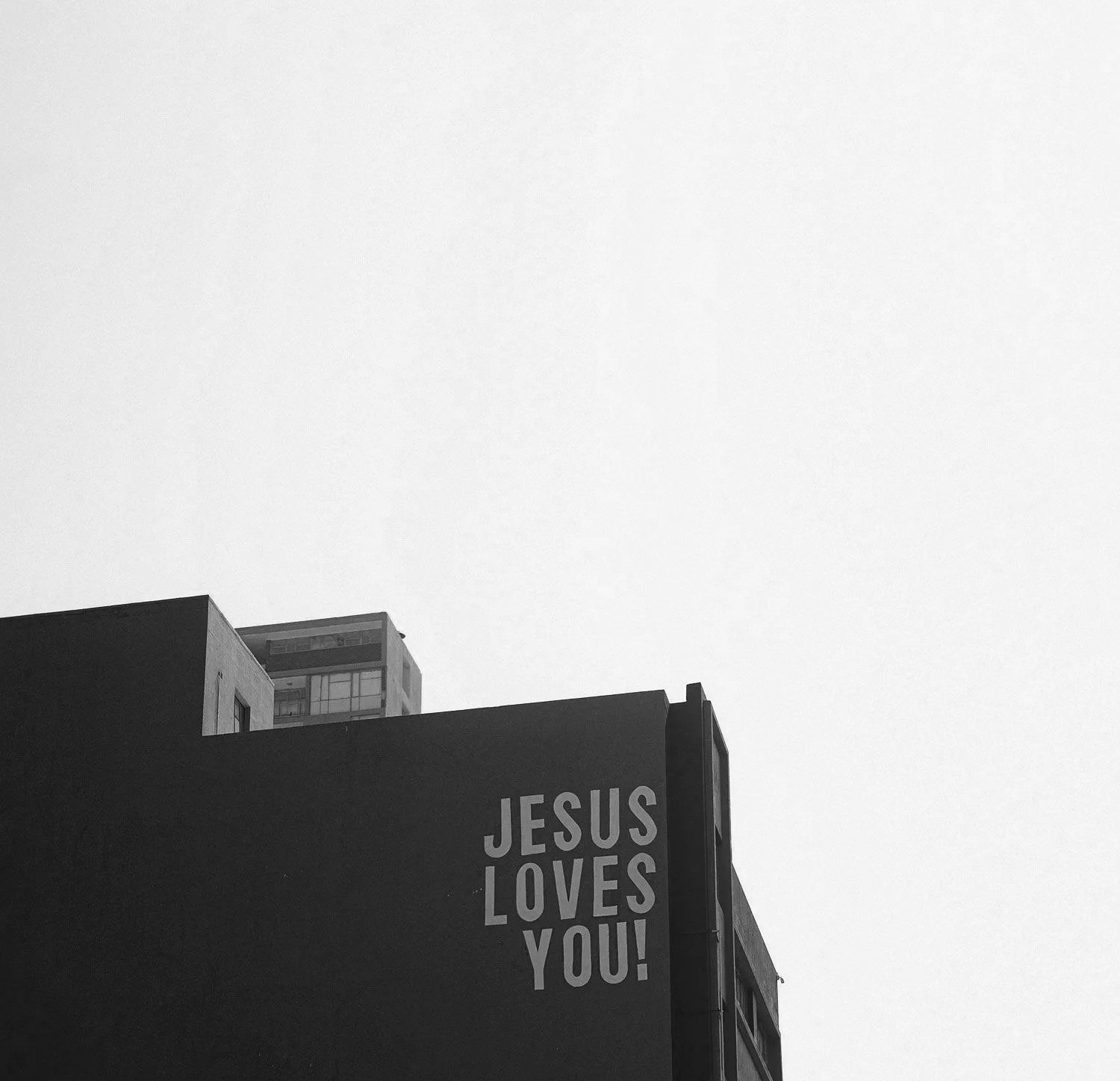 Black and white photo of a building with a sign that reads 'Jesus Loves You!'