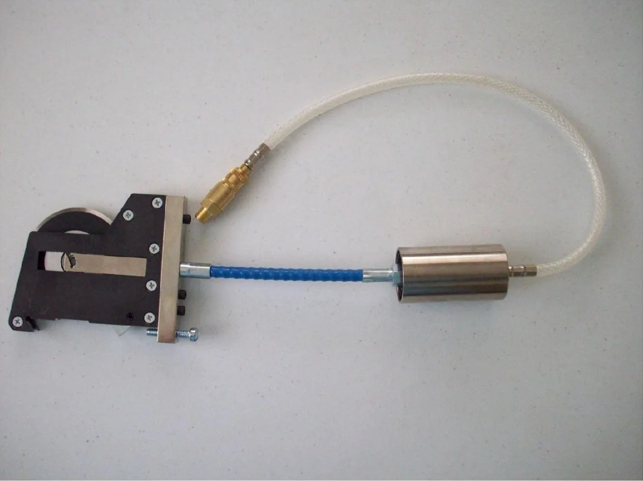 A mechanical device with a black metal component, a blue flexible tube, and a metallic cylindrical part connected with white and transparent tubing.