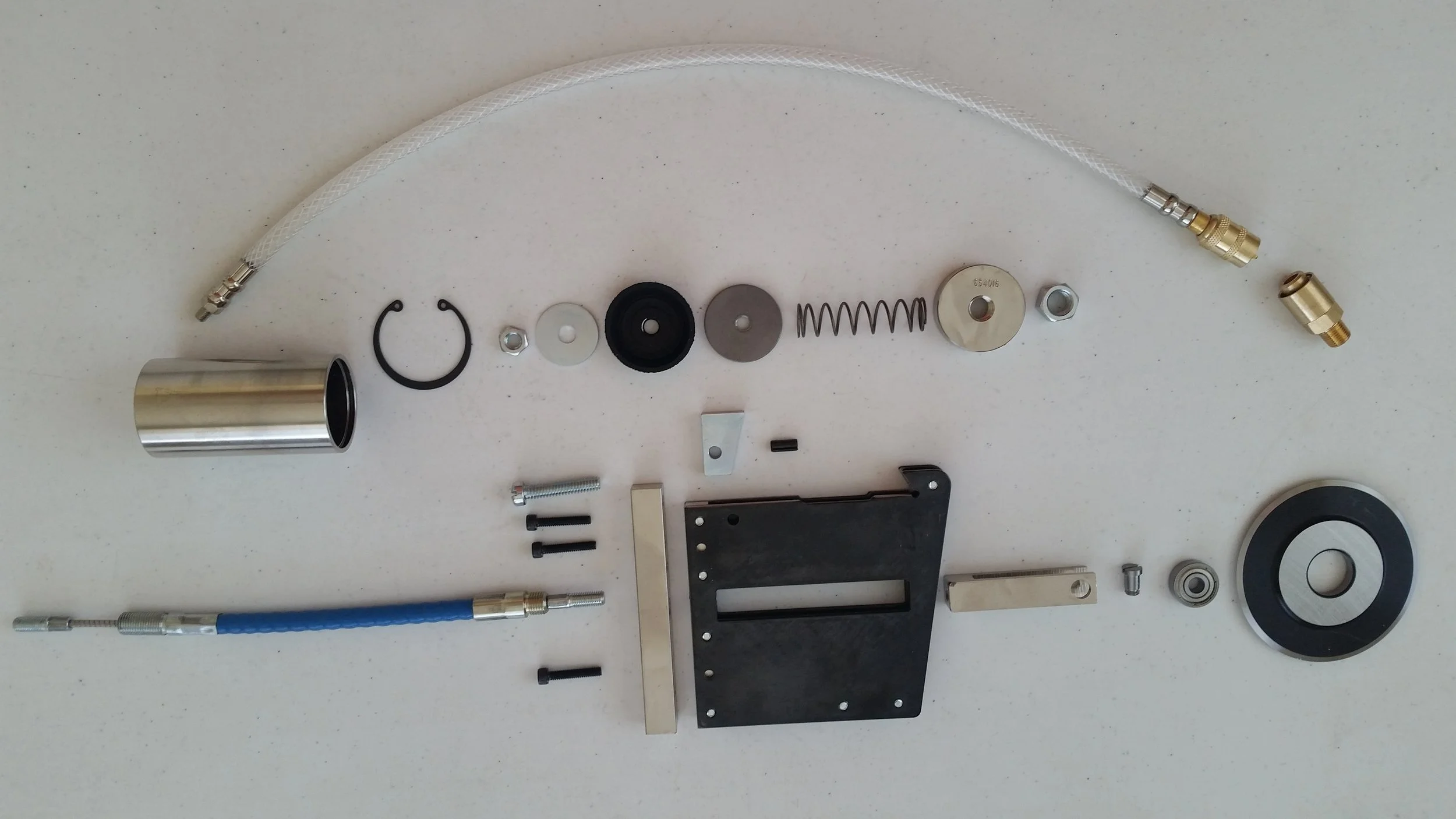 Various disassembled mechanical and electronic components arranged on a white surface, including a metal cylinder, washers, springs, screws, and a flexible braided hose.