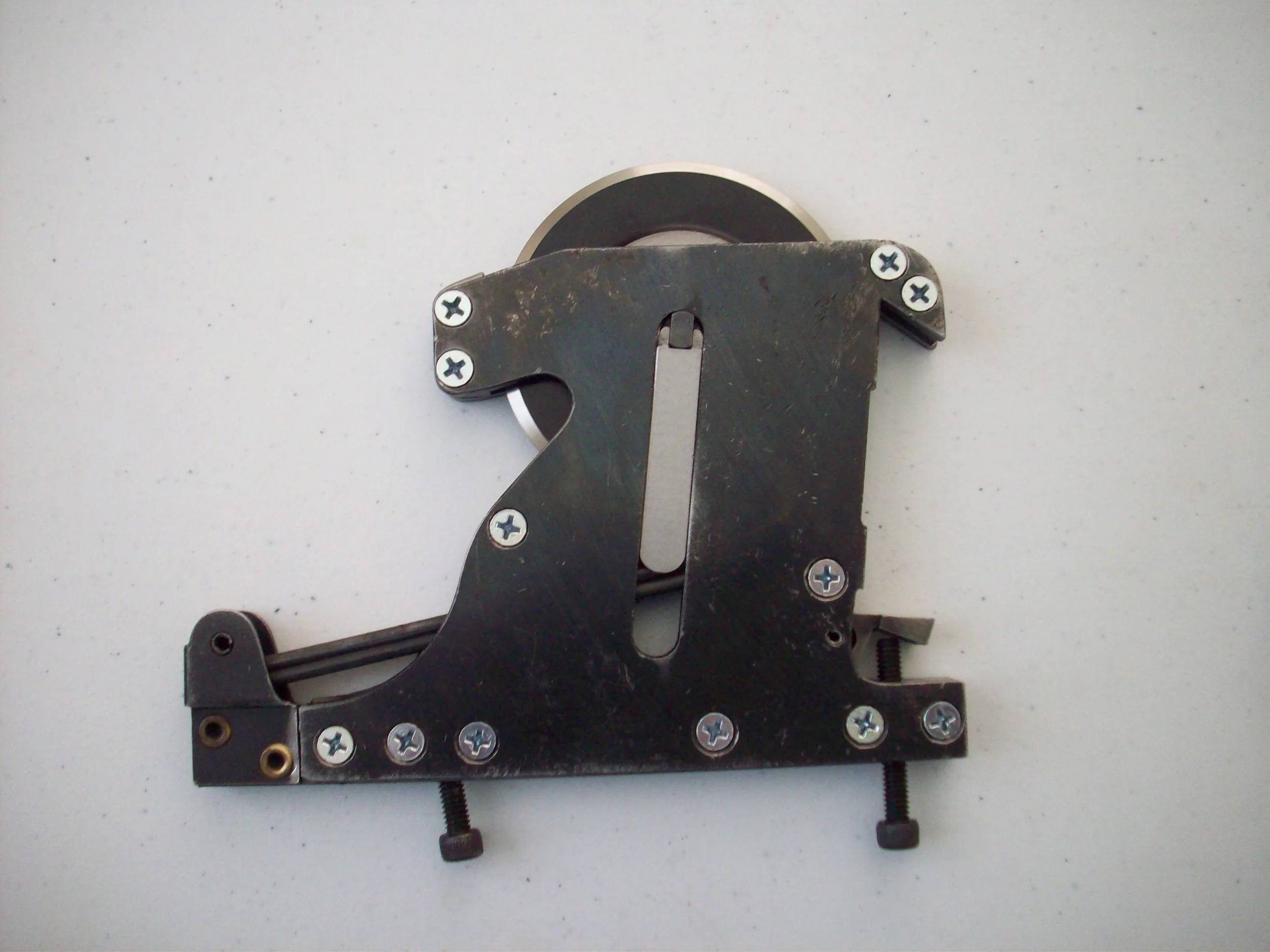 A metal component with screws, springs, and rollers, possibly part of a machine or tool, placed on a white surface.