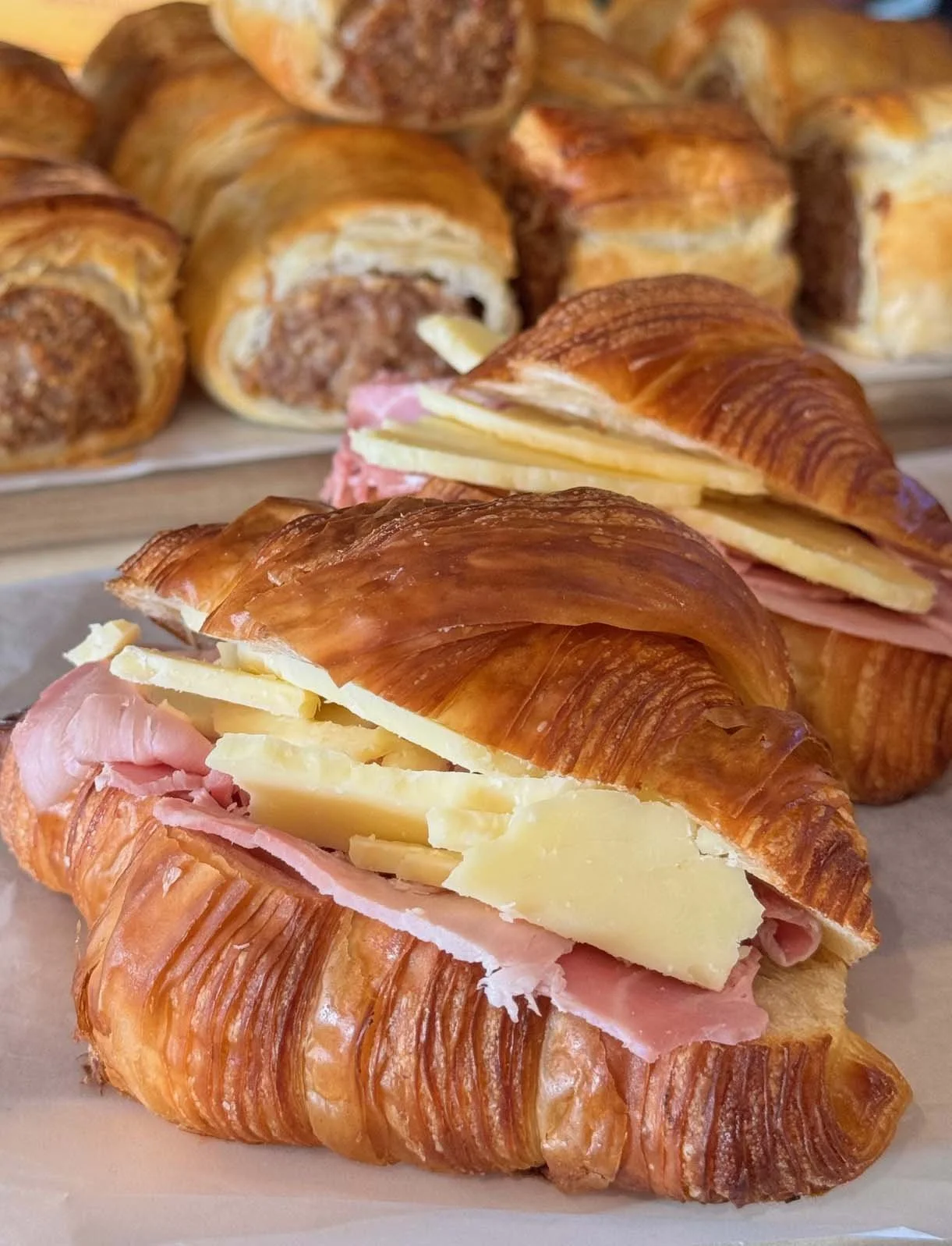 Close-up of a savoury croissant with cheese, ham, and slices of cheese on top, with more croissants in the background.