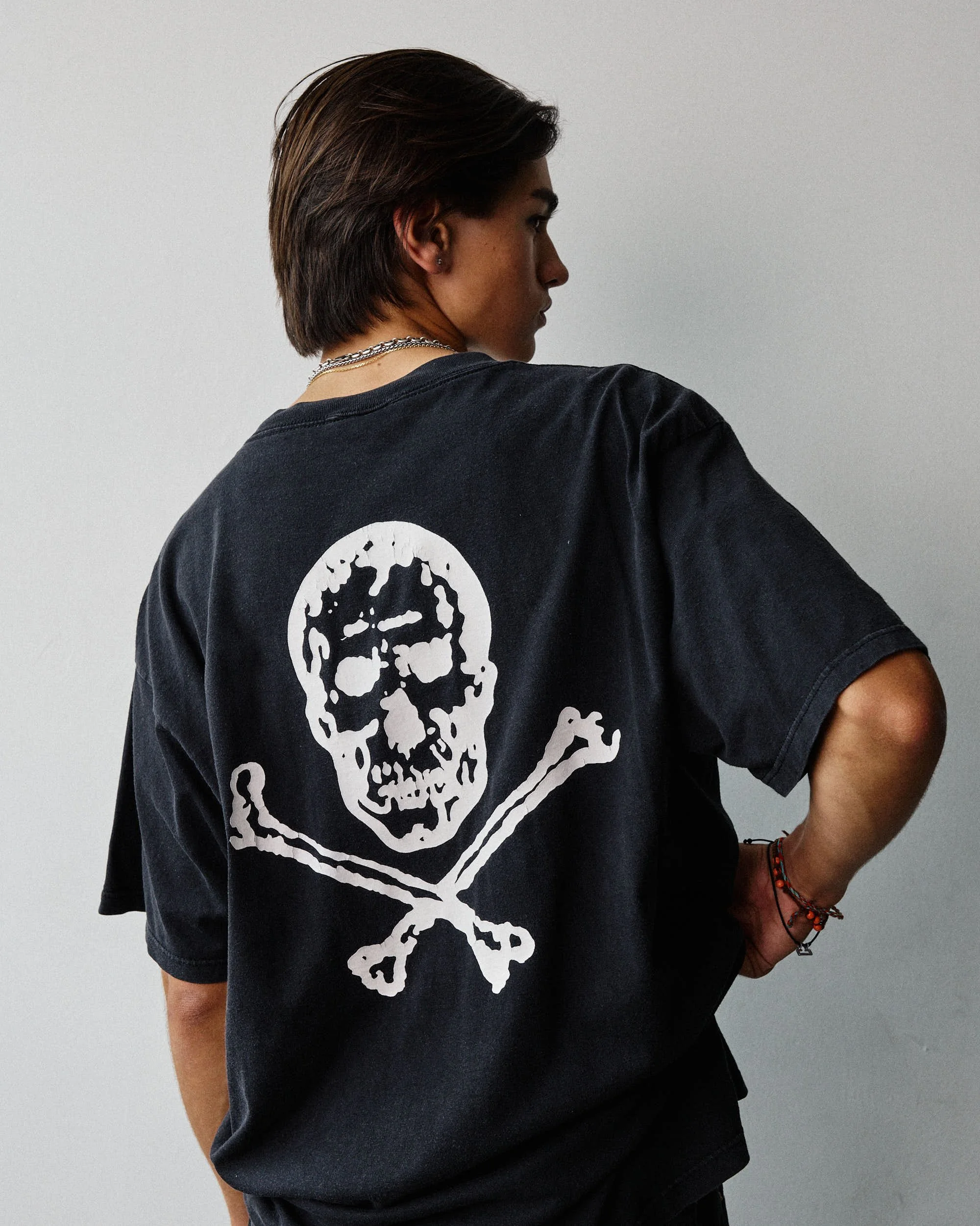 Person wearing a black T-shirt with a white skull and crossbones graphic on the back, facing sideways with one arm bent.