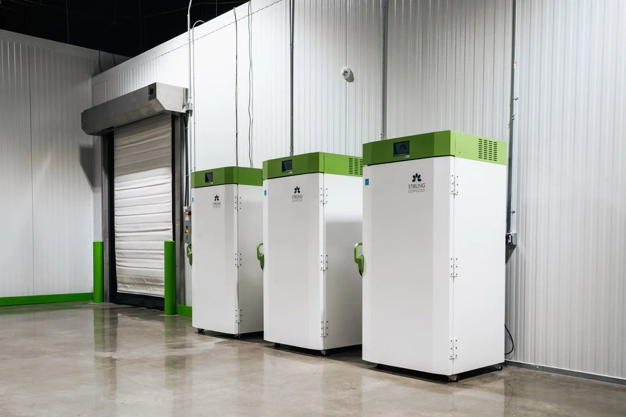 Three Stirling Ultracold cryogenic freezers in a clean room with a white roll-up door and metallic walls.