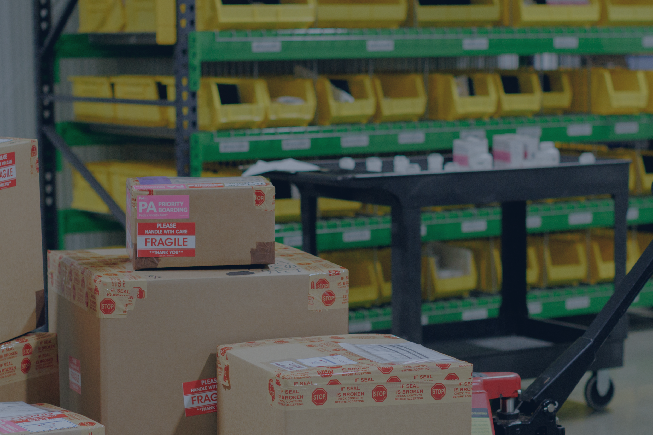 Stacked cardboard boxes with red 'fragile' and 'stop' warning labels in a warehouse setting.