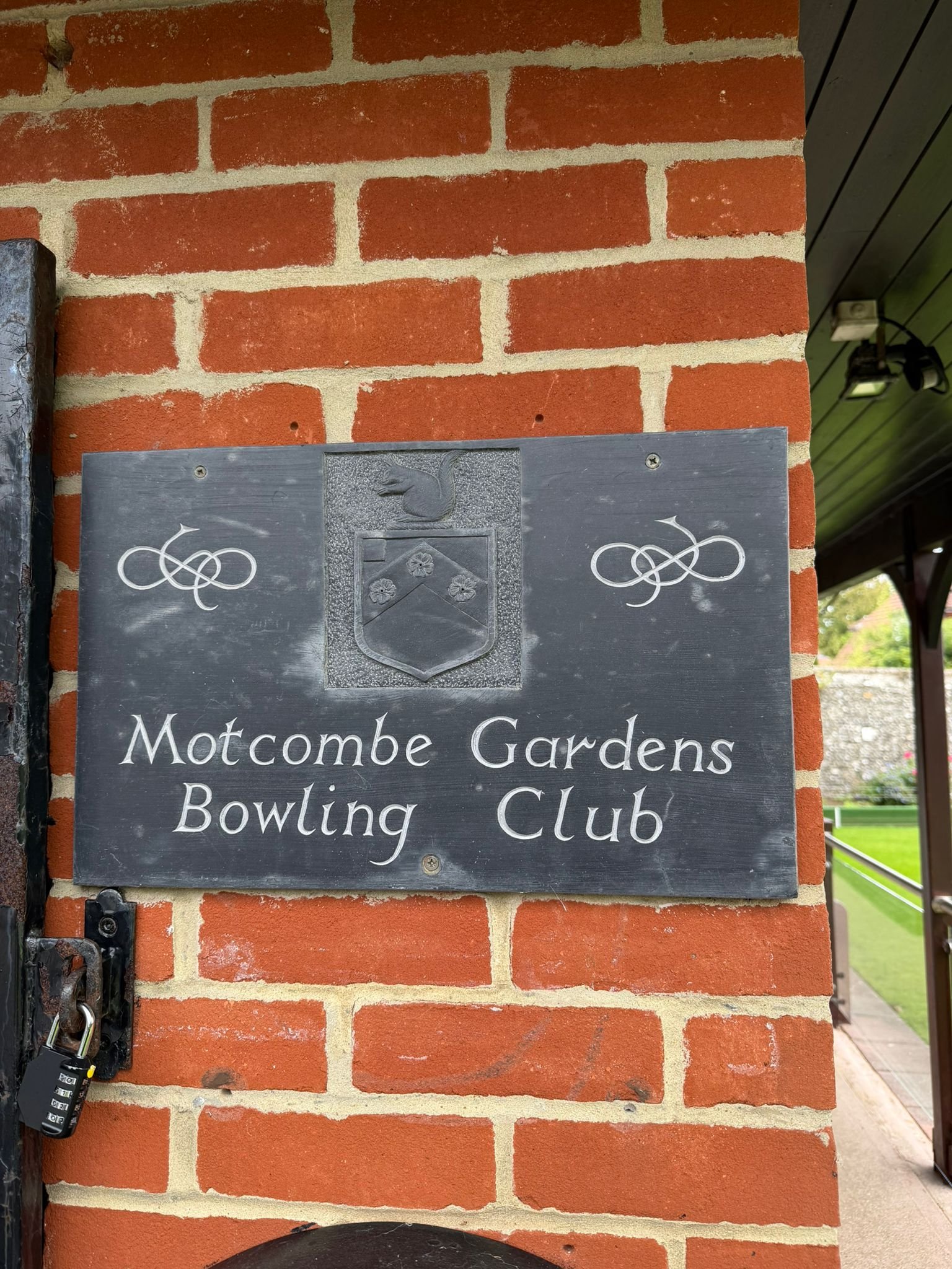 Black lawn bowls on green grass with the text 'Motcombe Gardens Bowls Club' overlaid.