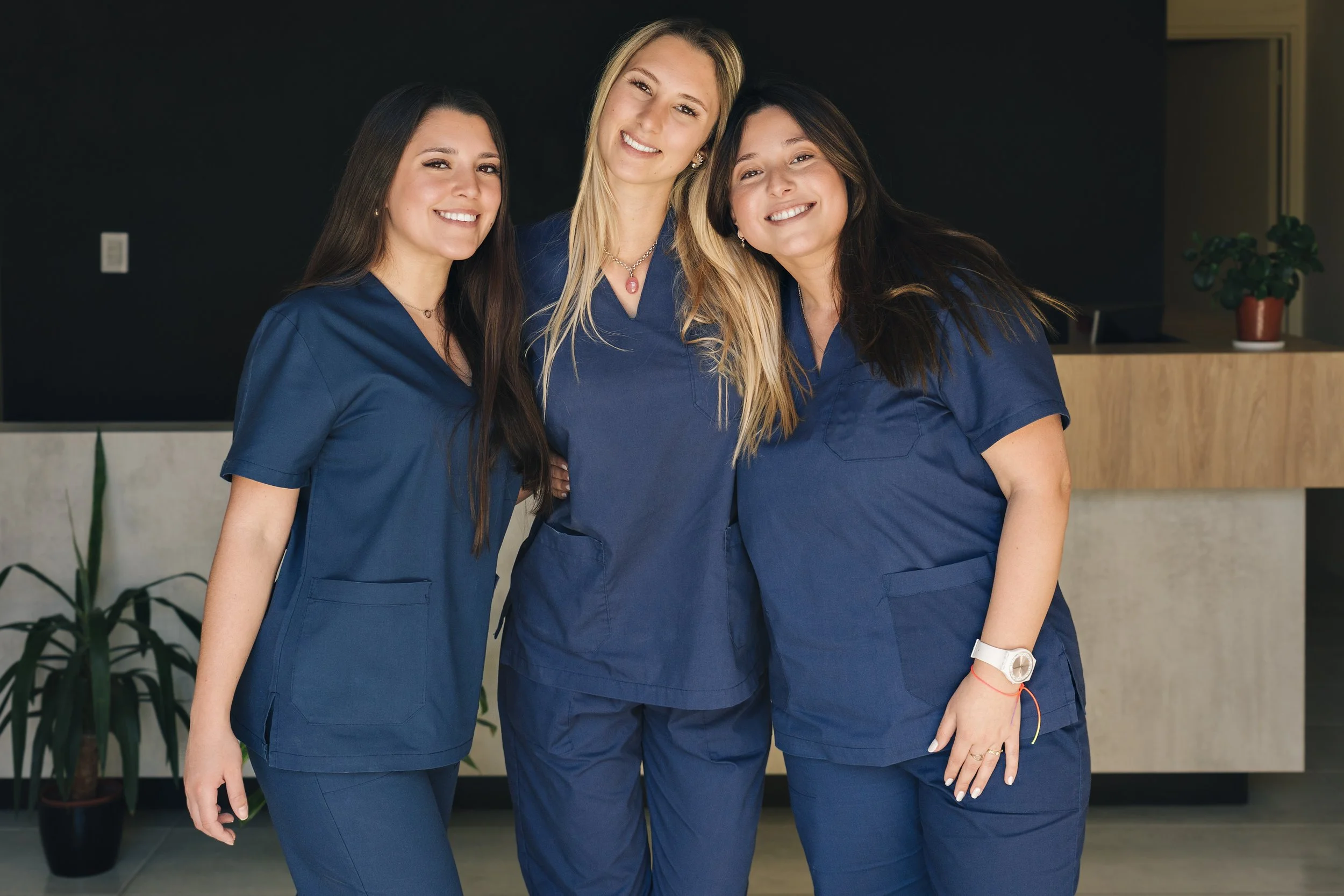 three women health care workers in navy scrubs smiling