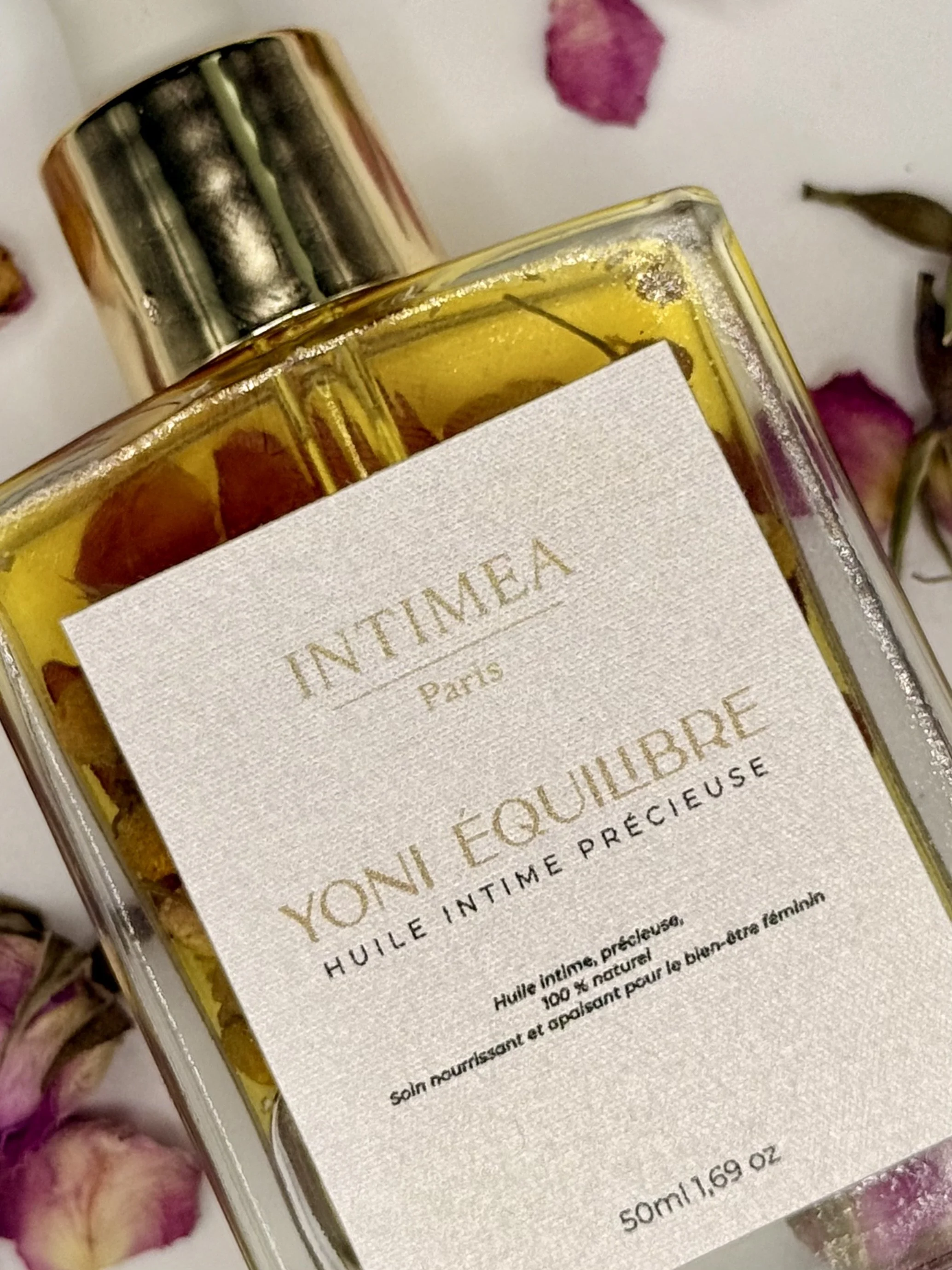 Bouteille d'huile intime Yoni Équilibre de la marque Intimina, d'une capacité de 50 ml, sur un fond de fleurs séchées rose et blanche.