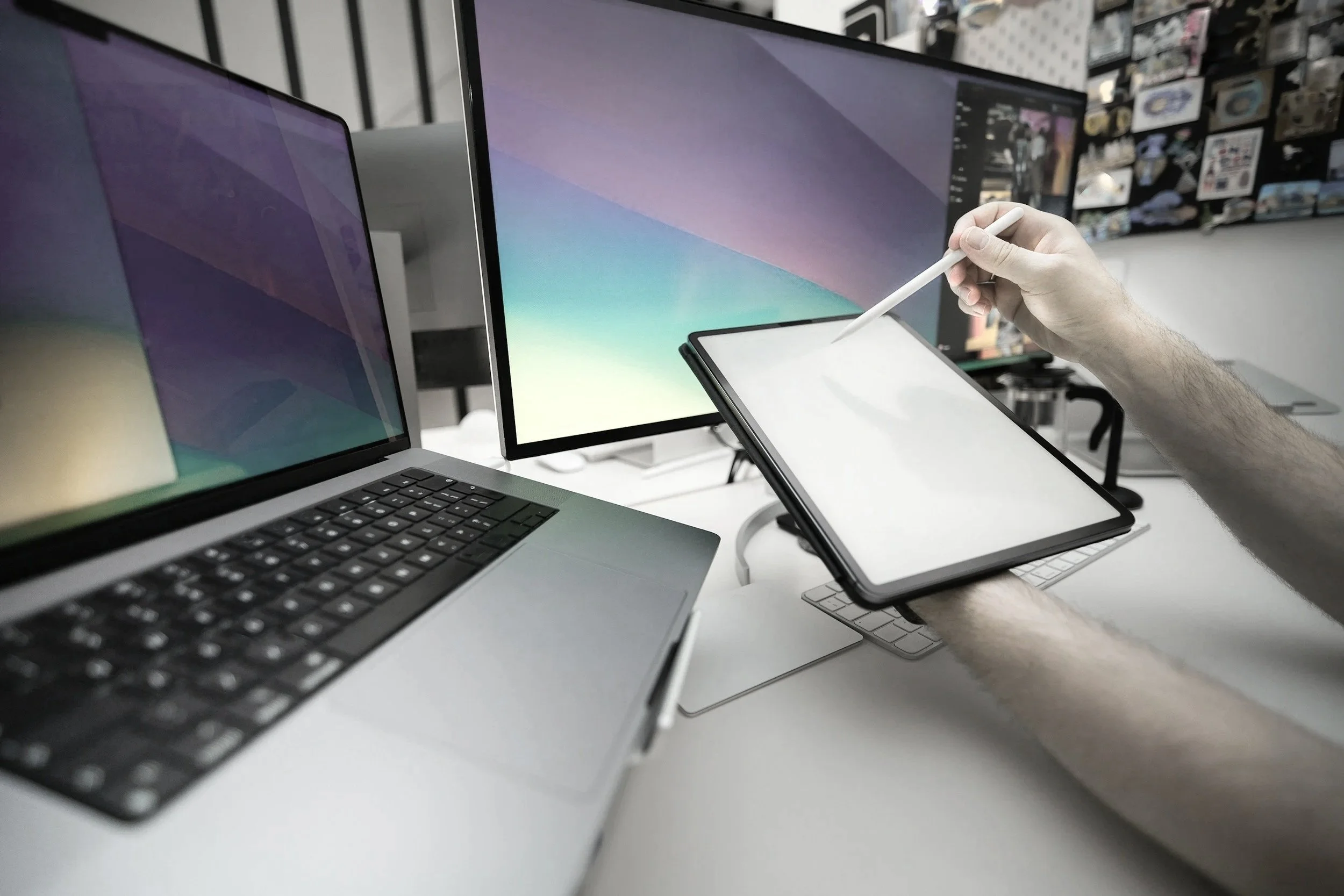 Person using a stylus to draw on a graphic tablet in front of multiple computer monitors and a laptop at a workspace.