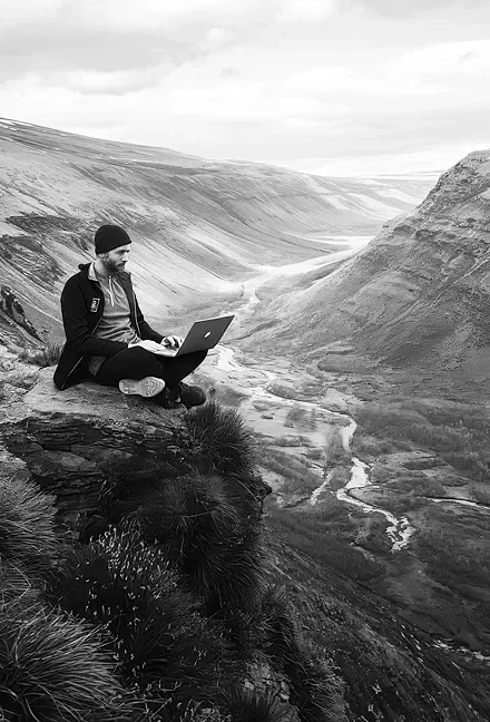 group practice web designer sitting on a mountain with laptop.
