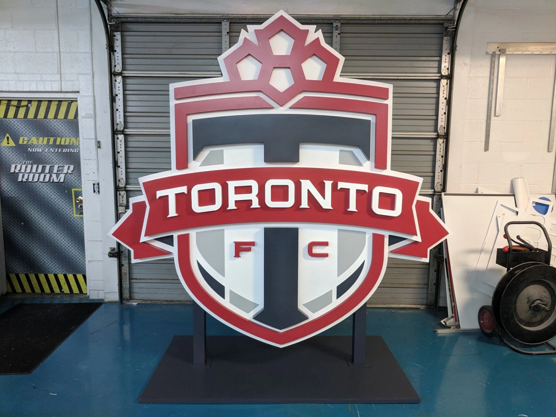 Large Toronto FC logo sign with a red, black, and white color scheme, including a shield shape and the text 'TORONTO FC' in the center.
