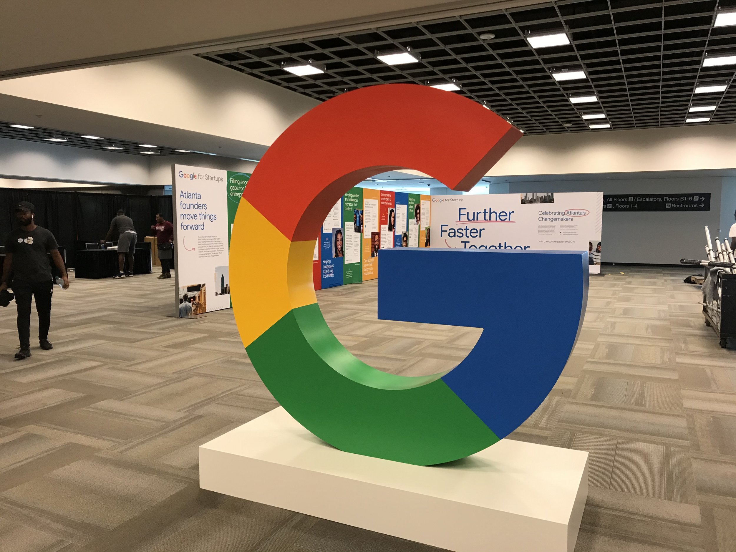 Large Google logo sculpture in an indoor conference space with informational displays in the background.