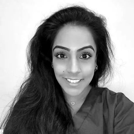 A woman with long black hair smiling at the camera, wearing a navy blue scrub top and small earrings.