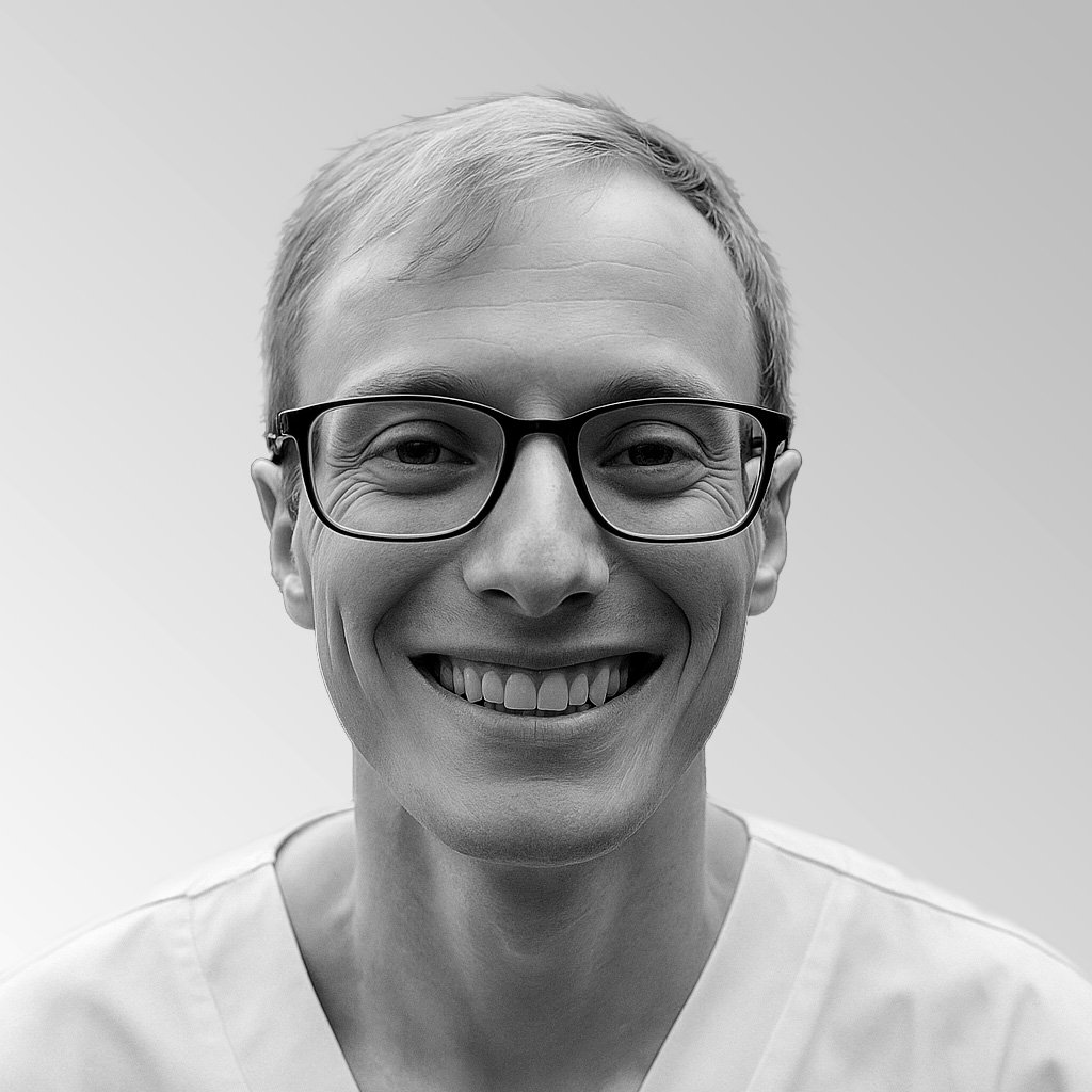 A person with glasses smiling outdoors with trees in the background.