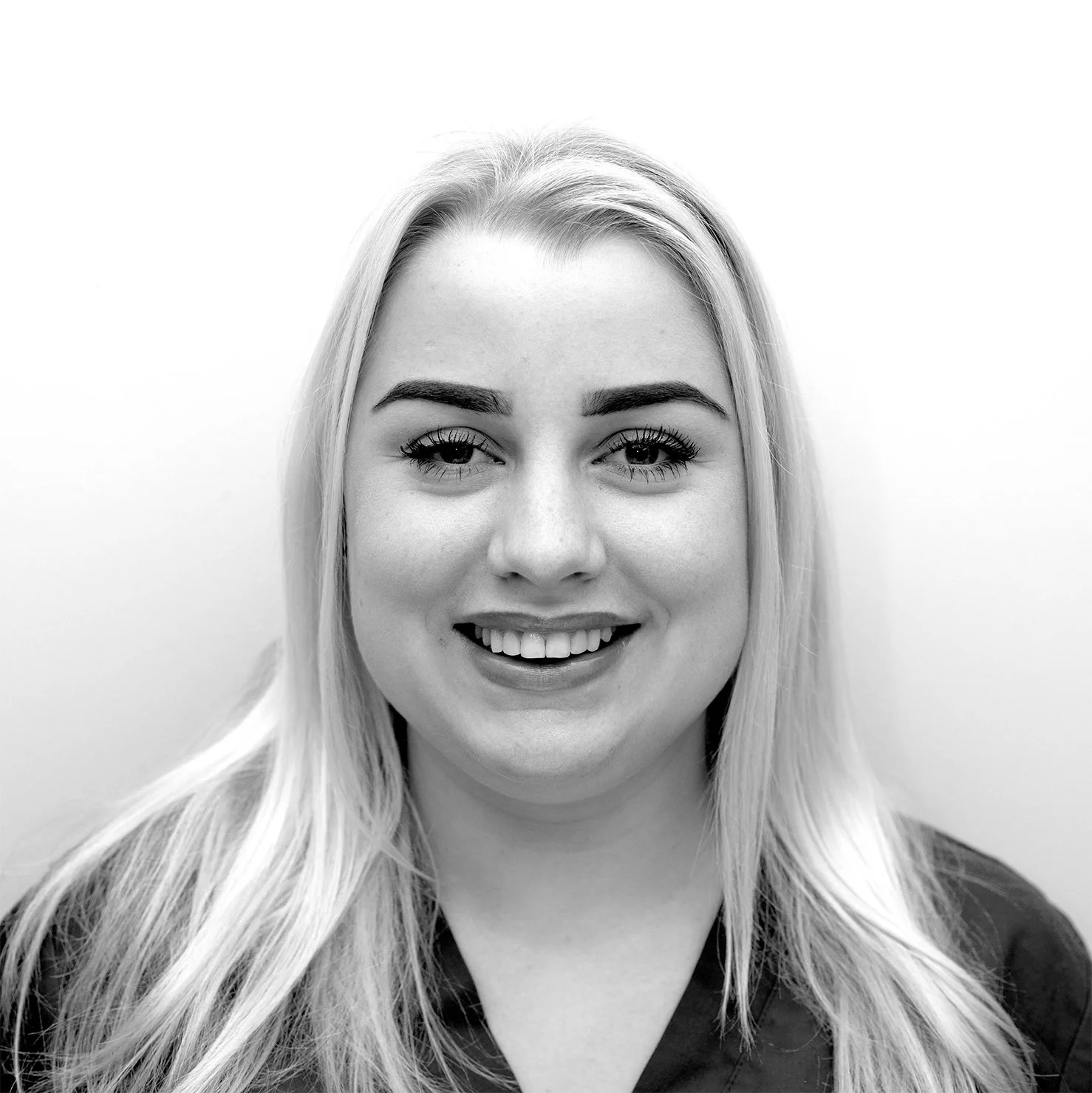 Black-and-white portrait of a smiling young woman with long, straight hair, wearing a dark top, against a plain background.